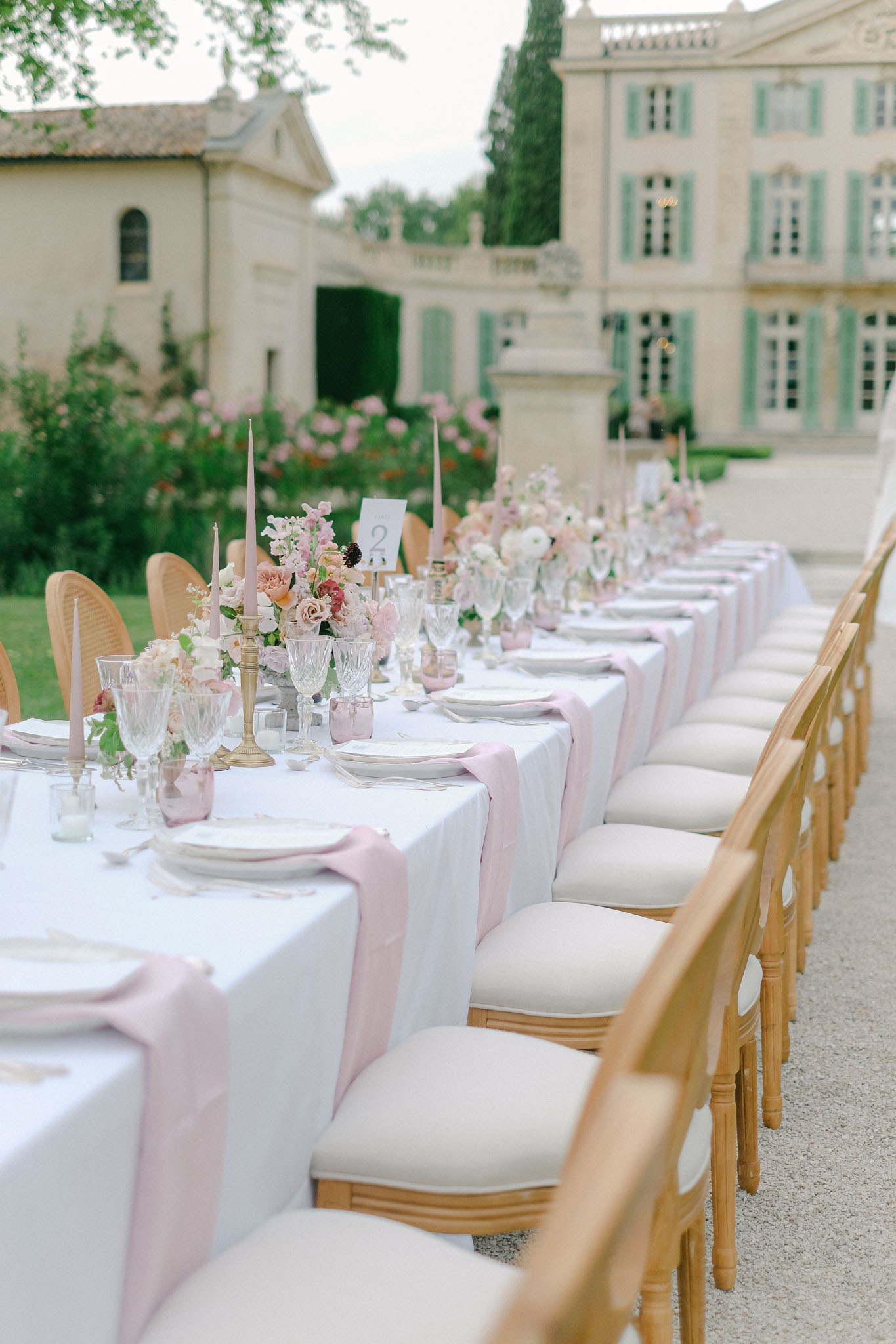 Long table with blush rose centerpieces brass candles Louis XVI chairs before sage-shuttered chateau