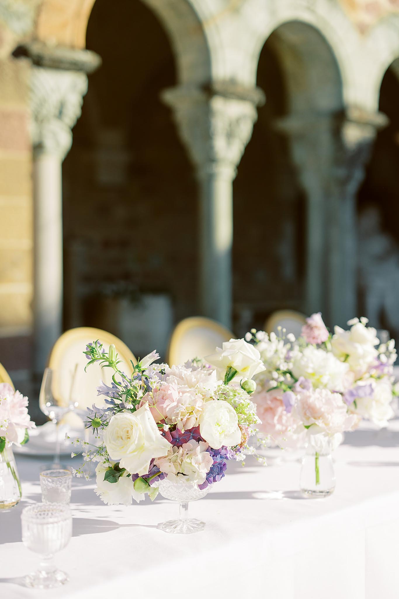 Reception table with blush peonies and lilac hydrangeas in glass compotes against stone arches