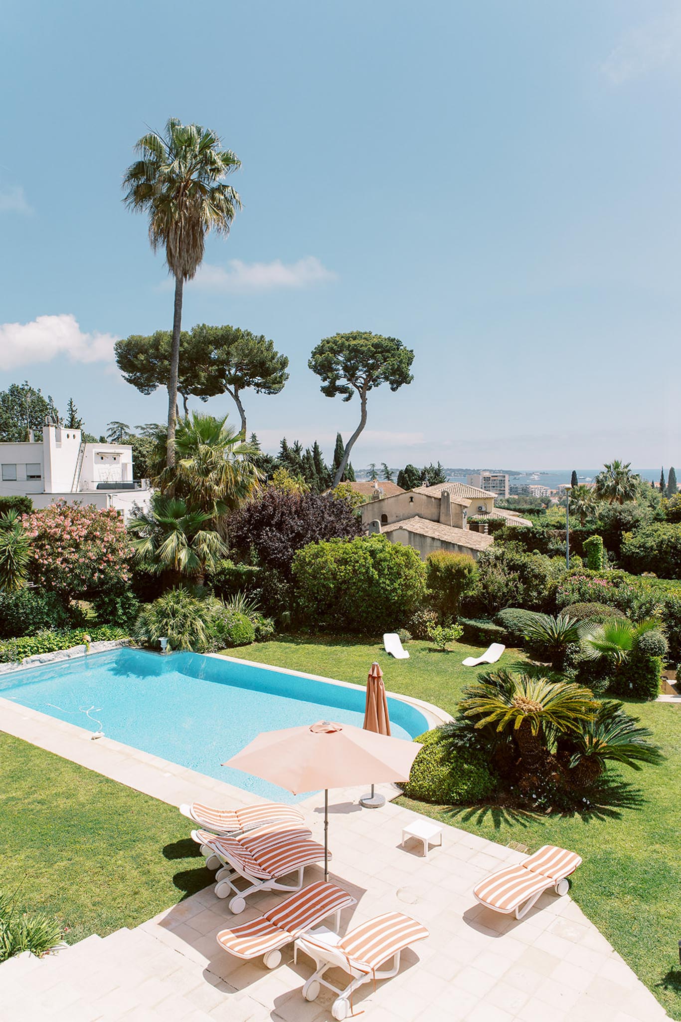 Elevated view of rectangular pool with striped sun loungers and Provencal stone building in hillside garden setting