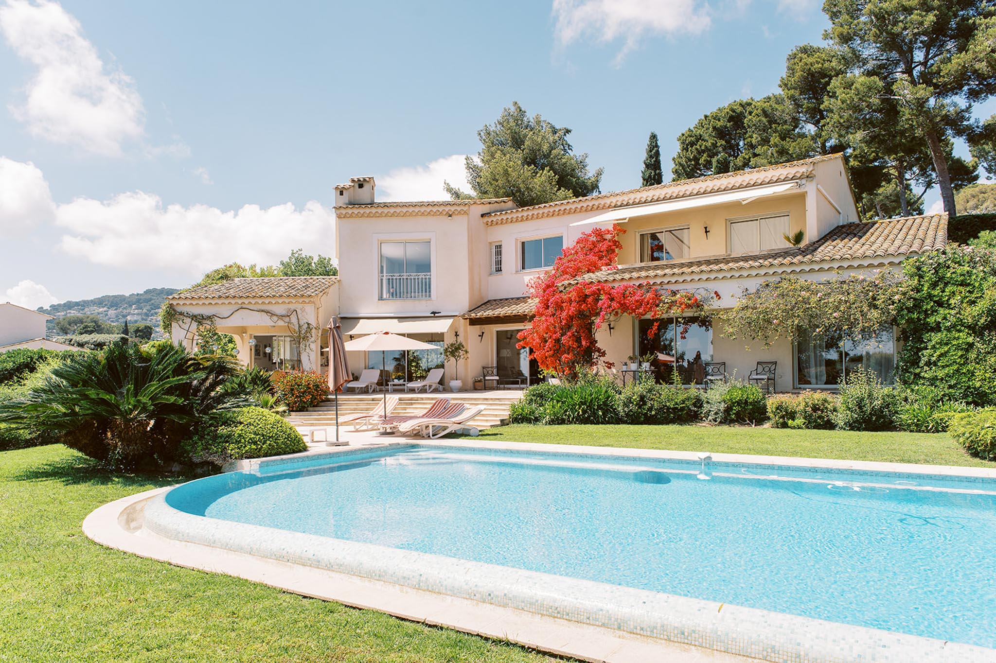 Provencal villa with cream walls and bougainvillea viewed from oval swimming pool and garden