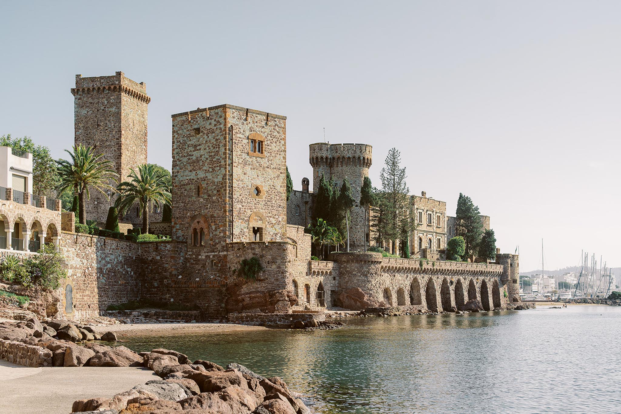 Medieval stone castle with crenellated towers and Moorish arches on waterfront with marina behind