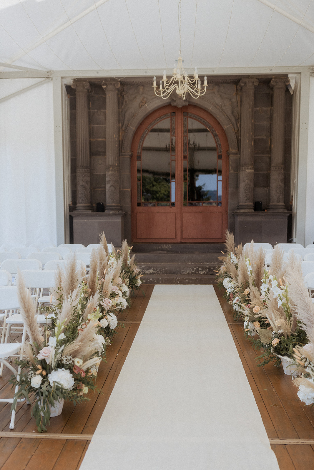 Ceremony aisle under white marquee with pampas grass and hydrangea arrangements leading to stone archway