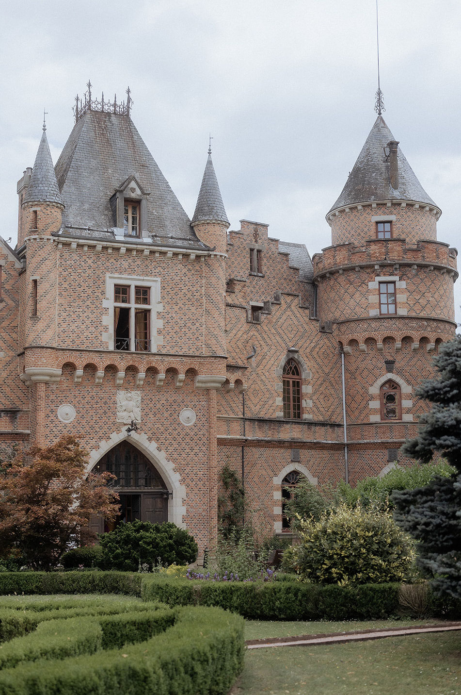Gothic-Revival chateau with conical turrets, pointed arches, and geometric boxwood parterre in foreground