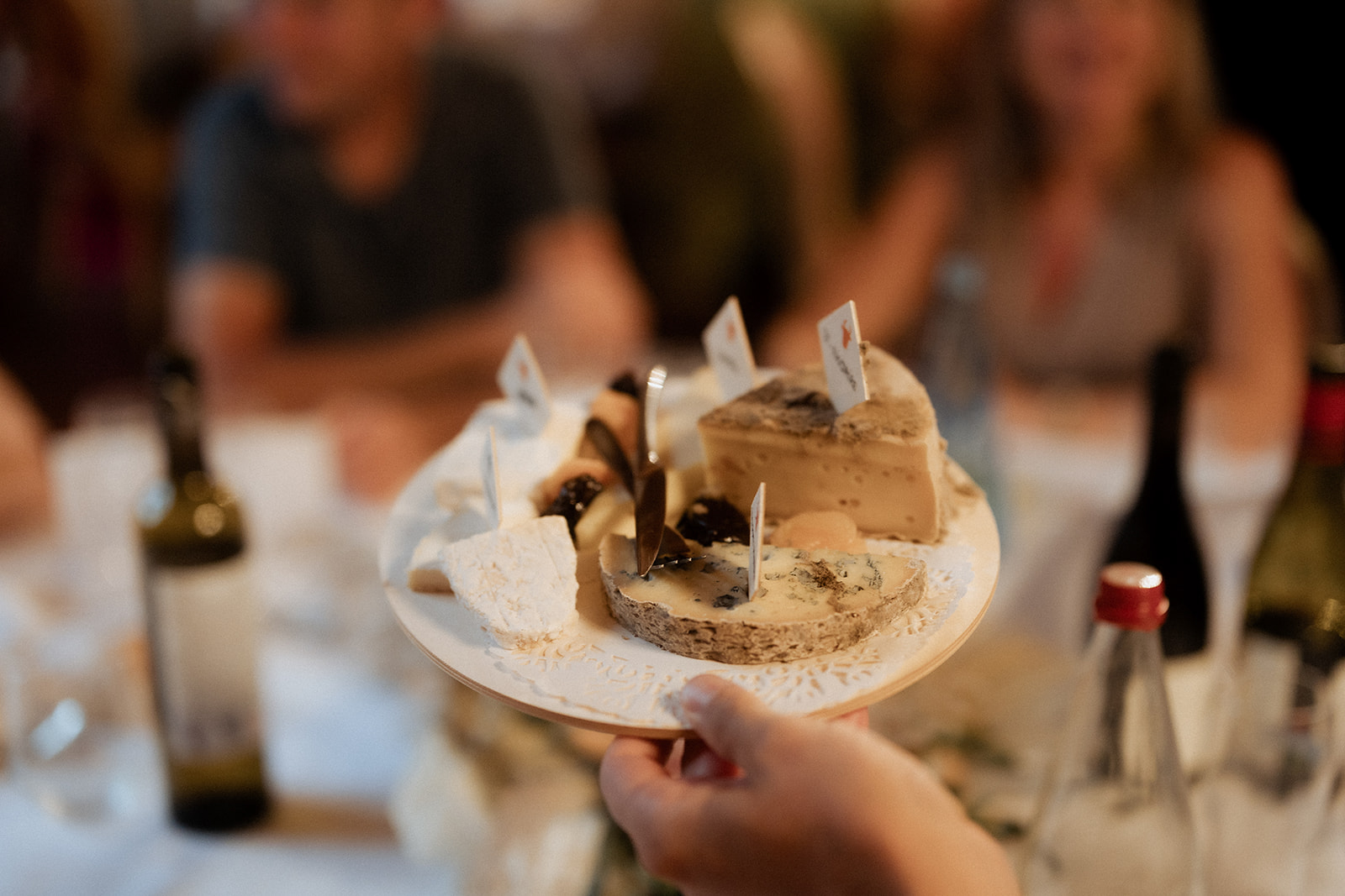 French cheese board with soft, blue, and firm cheeses on wooden board held up during wedding reception dinner