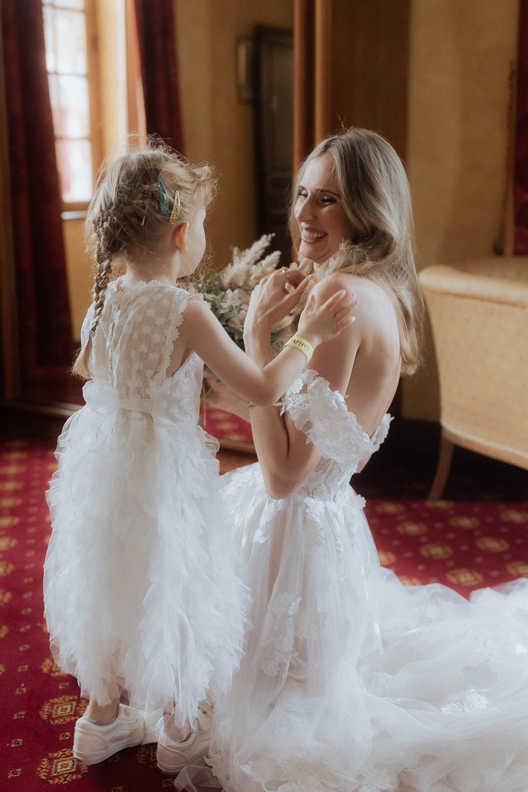 Bride in off-shoulder lace gown crouching to hold hands with flower girl in white ruffle dress