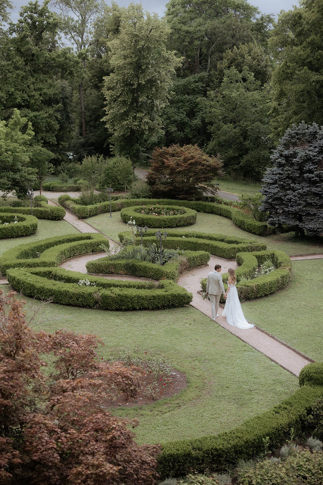Aerial view of couple walking through ornate boxwood parterre garden at French chateau