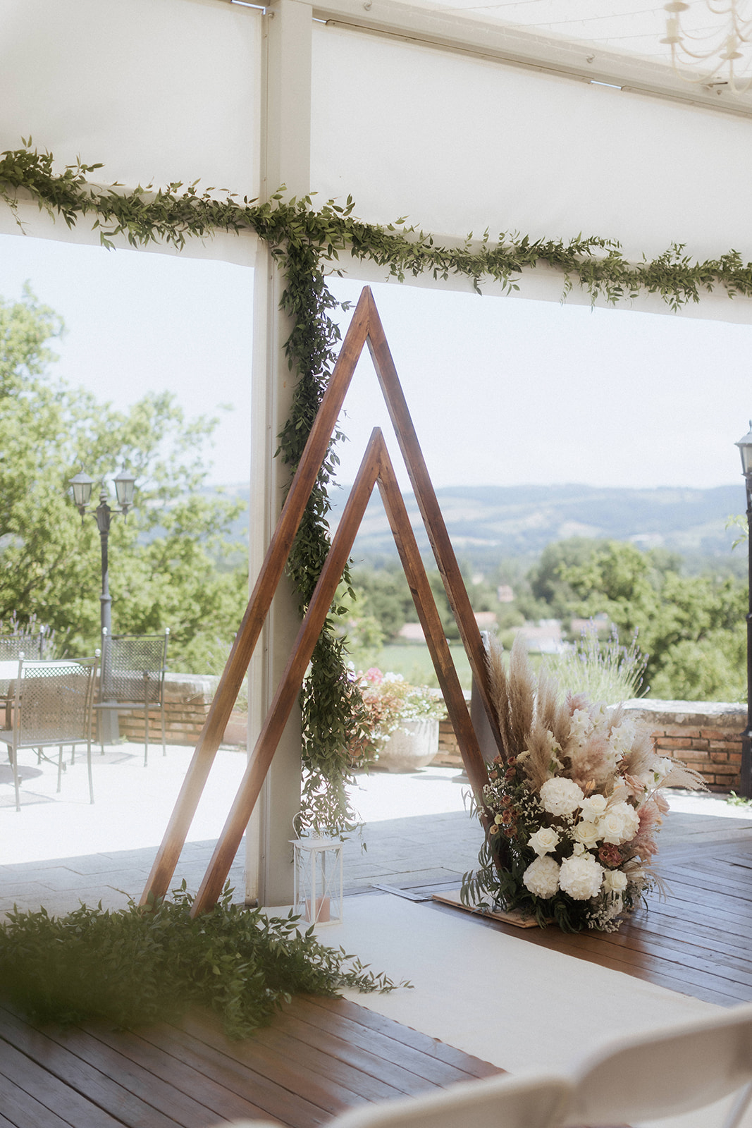 Boho ceremony altar with twin wooden A-frame arches, pampas grass, and white florals in open marquee