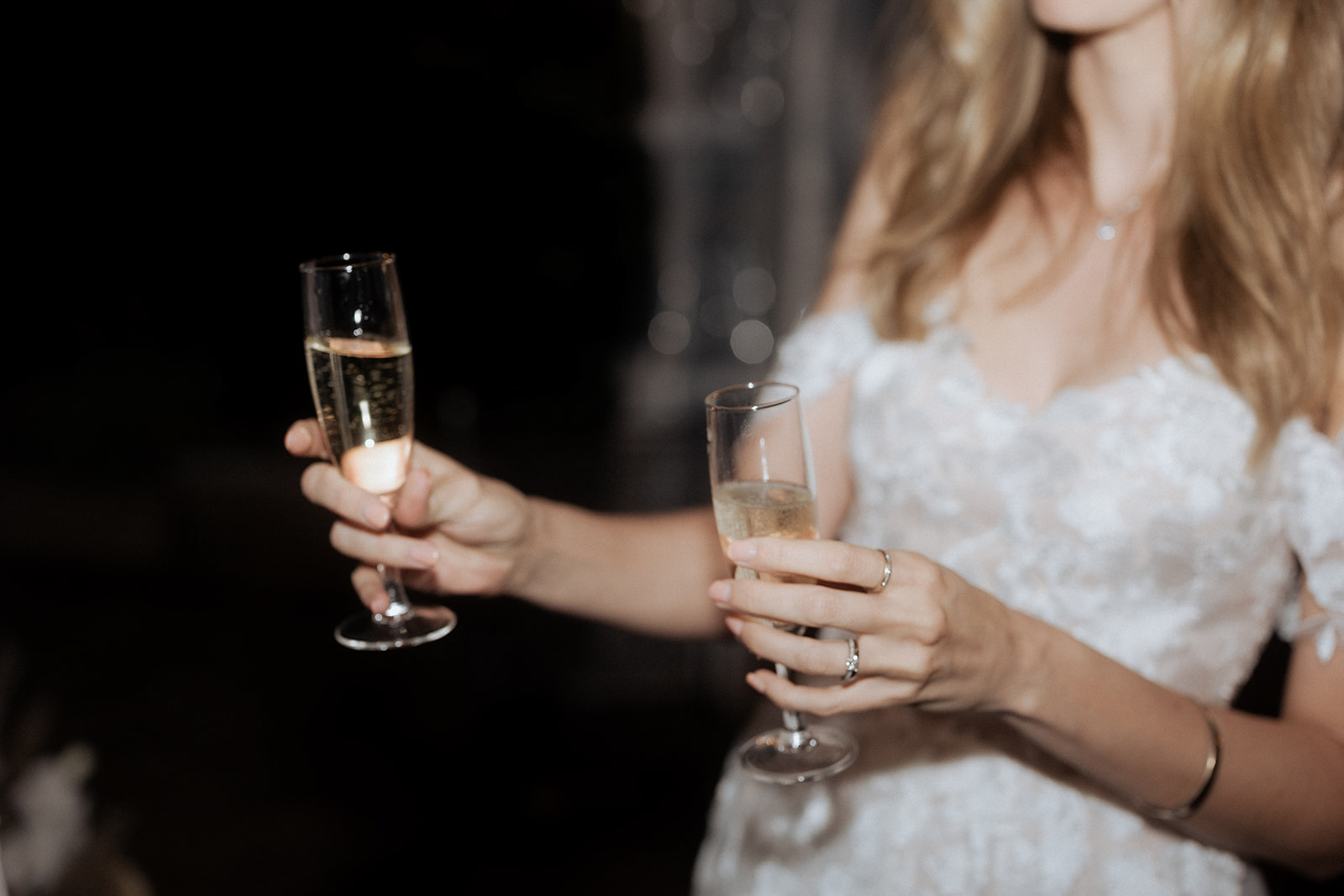Bride in white lace dress holding champagne flute during reception toast in low-light setting