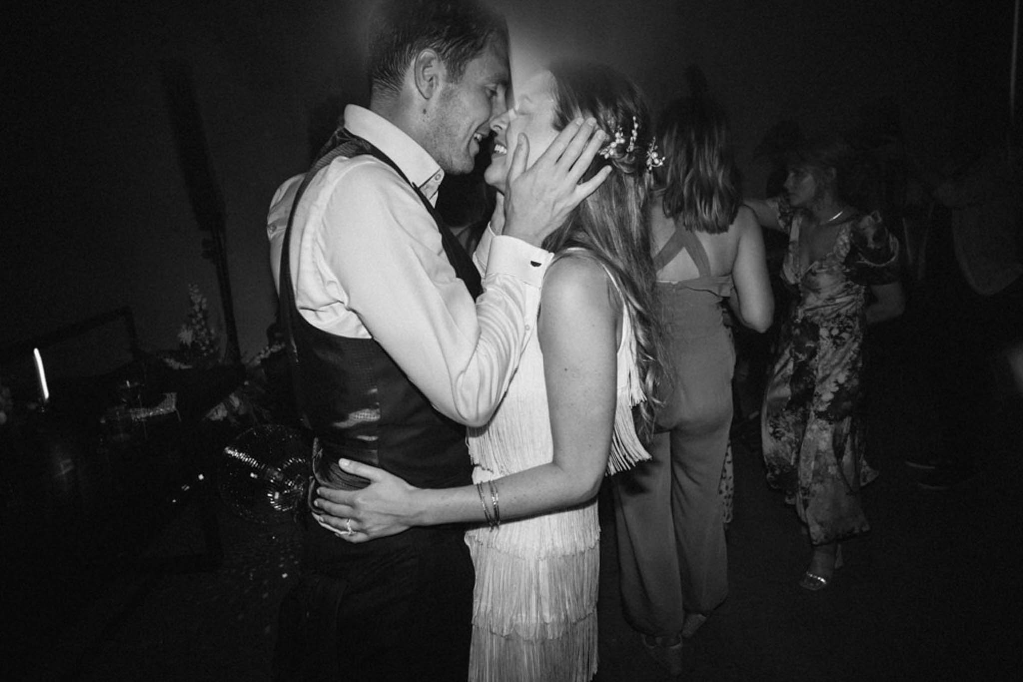 Black and white couple laughing on dance floor, bride in fringed reception dress with floral hair accessory