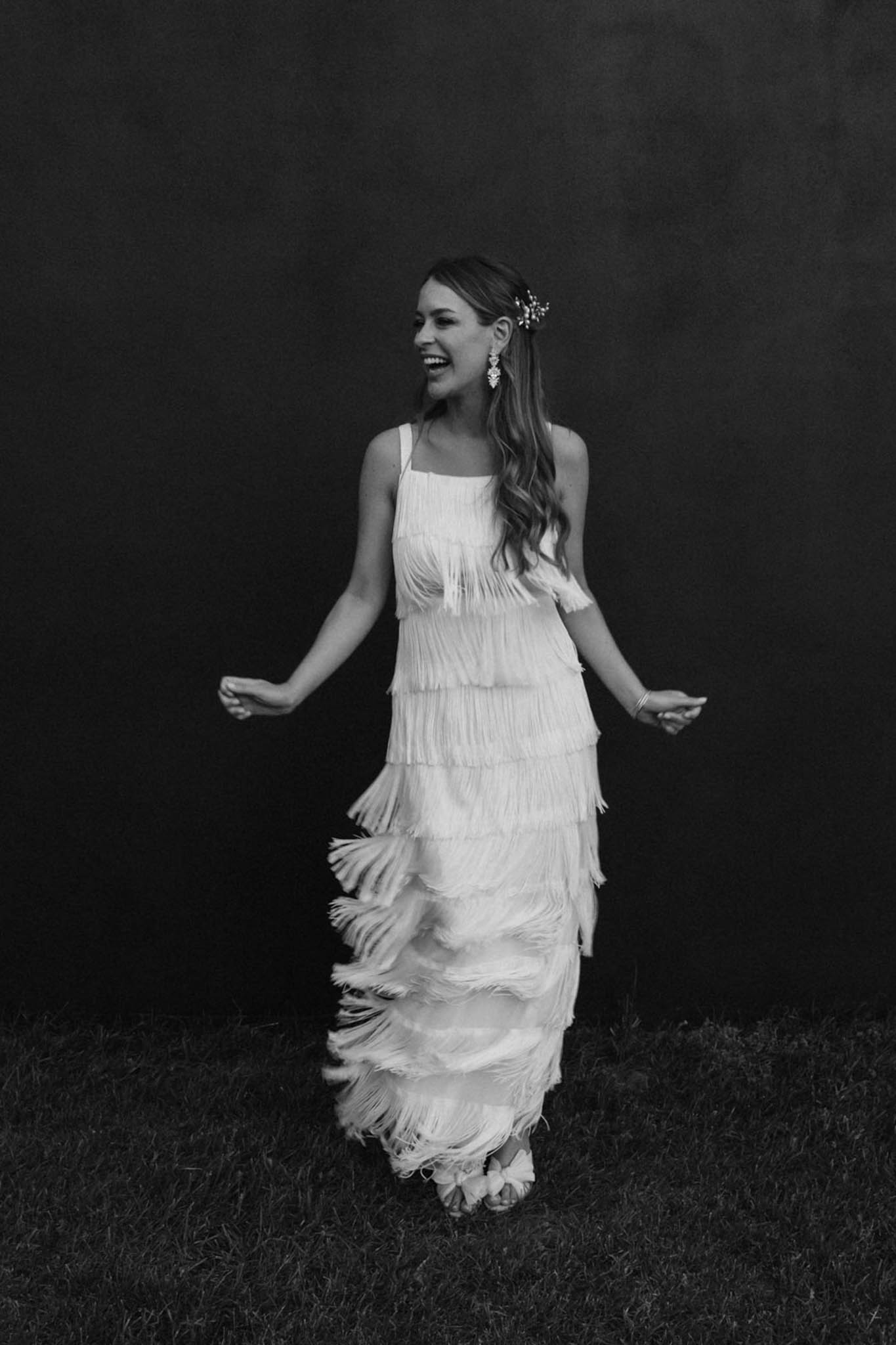 Black and white portrait of bride laughing in tiered fringe wedding dress with 1920s flapper styling outdoors
