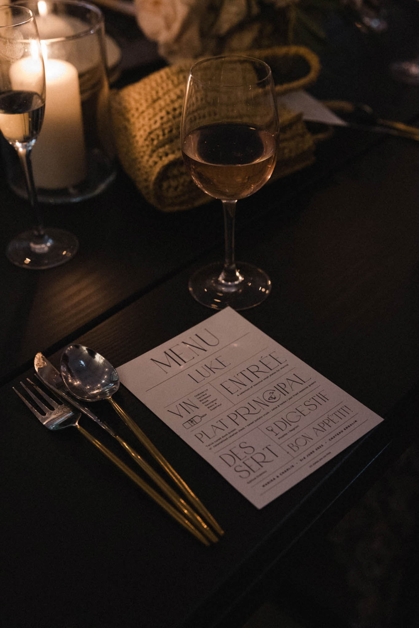 Bold graphic menu card on black linen with gold cutlery rose wine and candlelight at Chateau Engalin