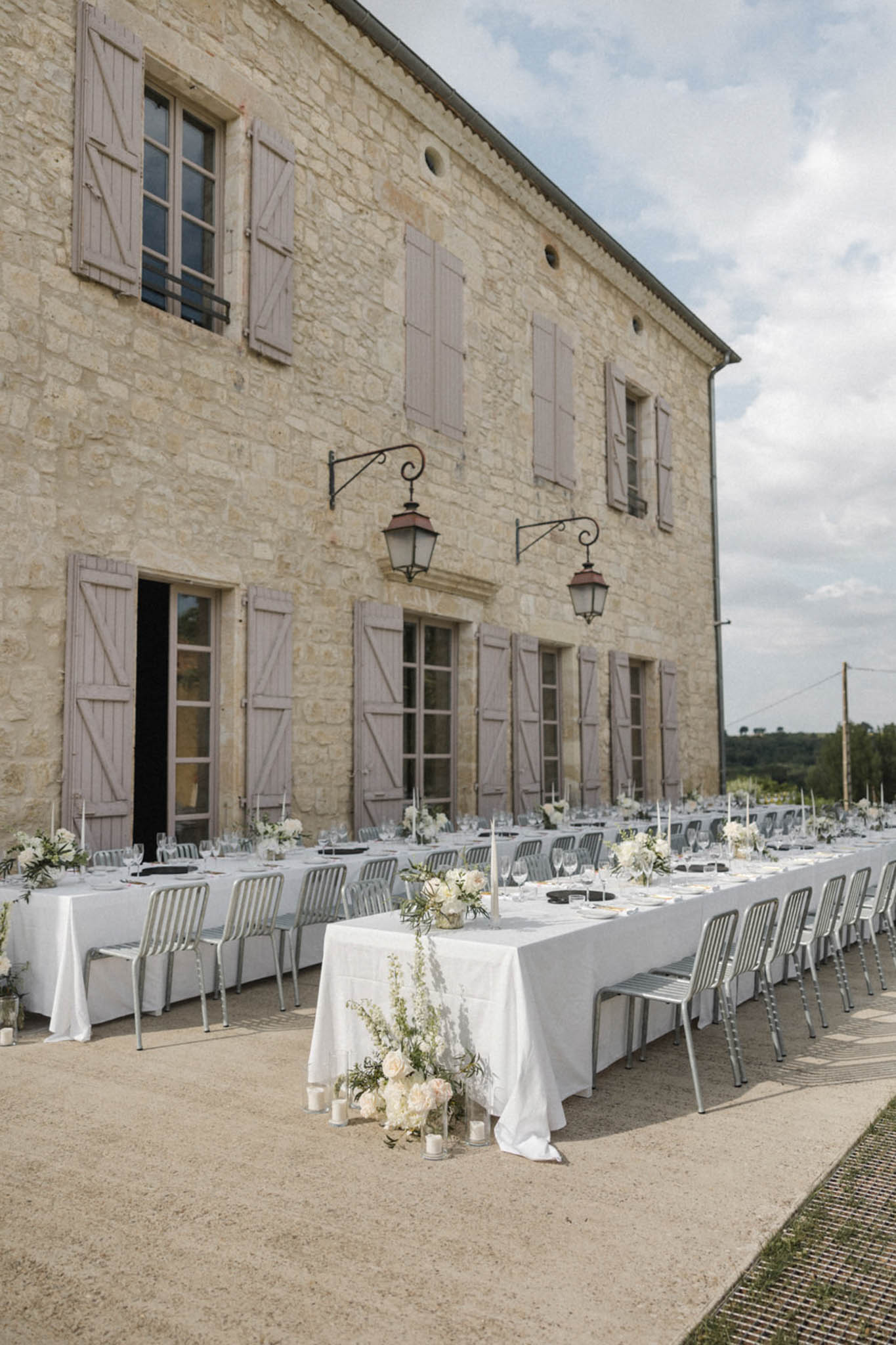 Outdoor wedding reception with long banquet tables, ivory and blush peony centerpieces, and taper candles along French lim...
