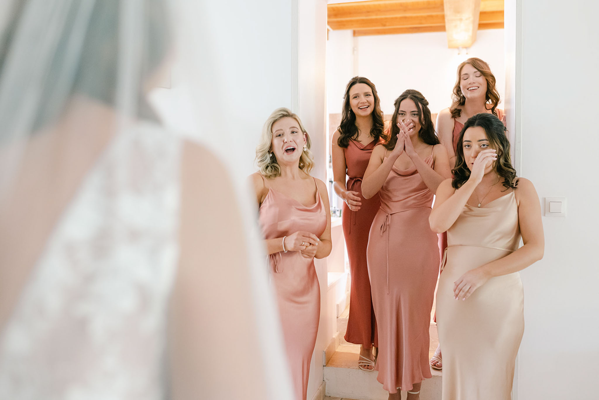 Bridesmaids in mismatched satin dresses react emotionally seeing the bride in her gown for the first time