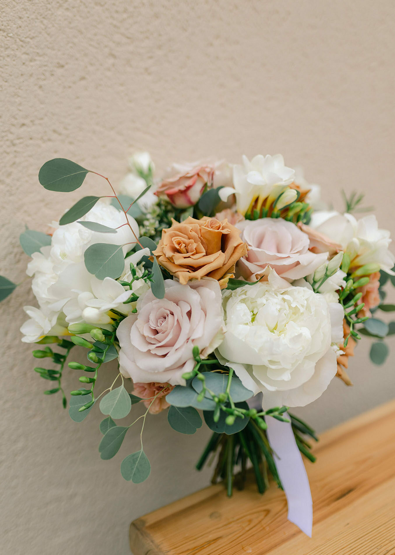 Bridal bouquet of white peonies dusty mauve roses caramel blooms and eucalyptus tied with lavender satin ribbon