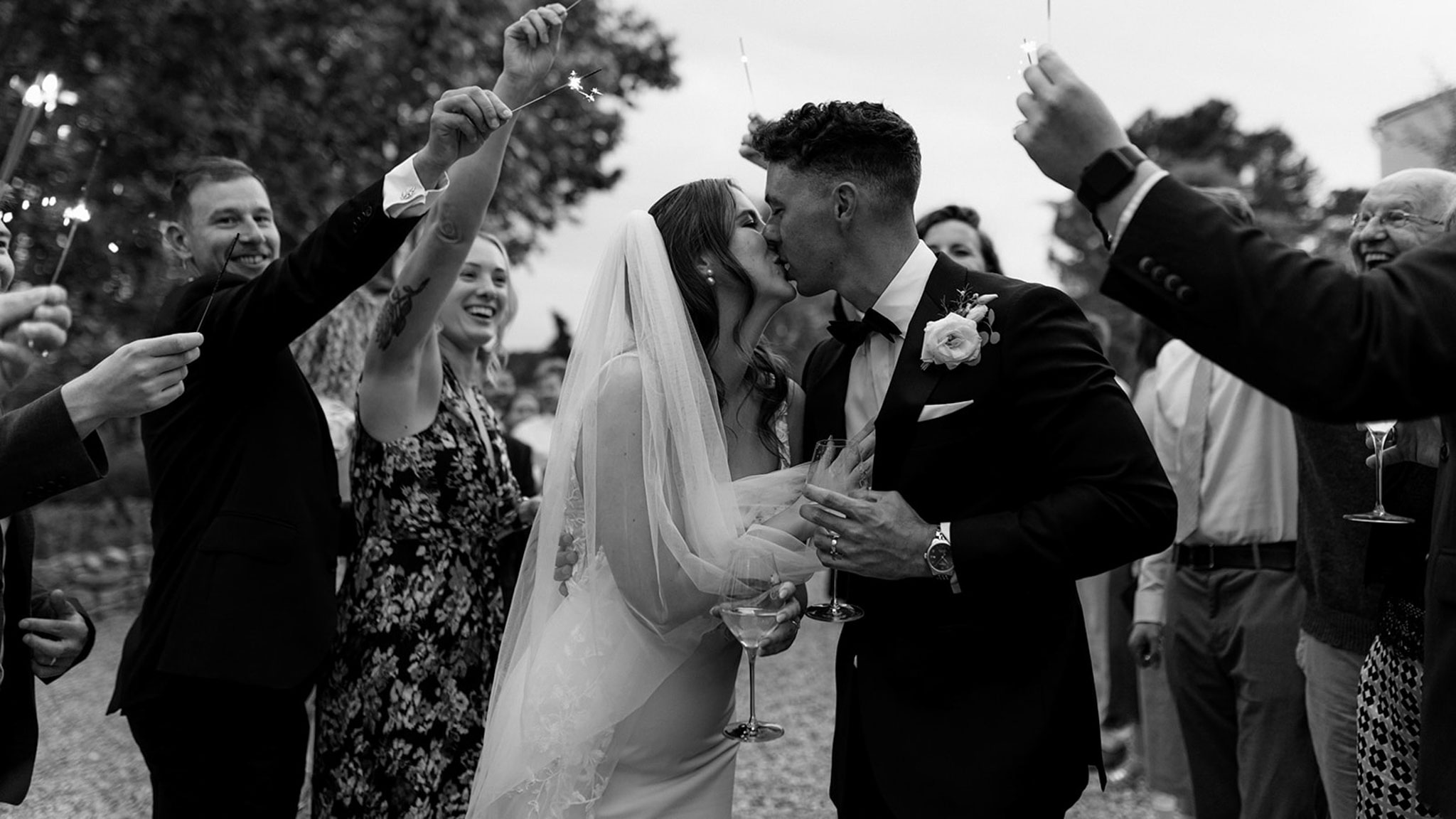 Black and white sparkler send-off with bride and groom kissing holding champagne coupes