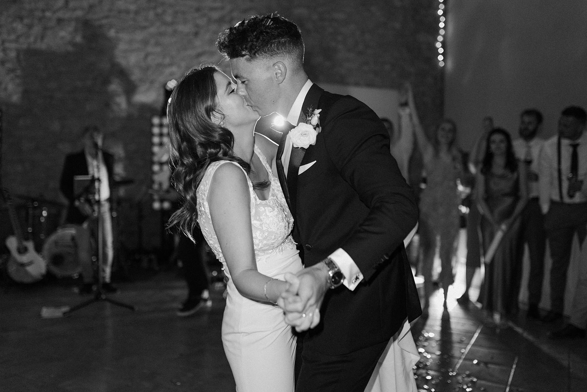 Black and white first dance kiss with live band and cheering guests in rustic stone venue