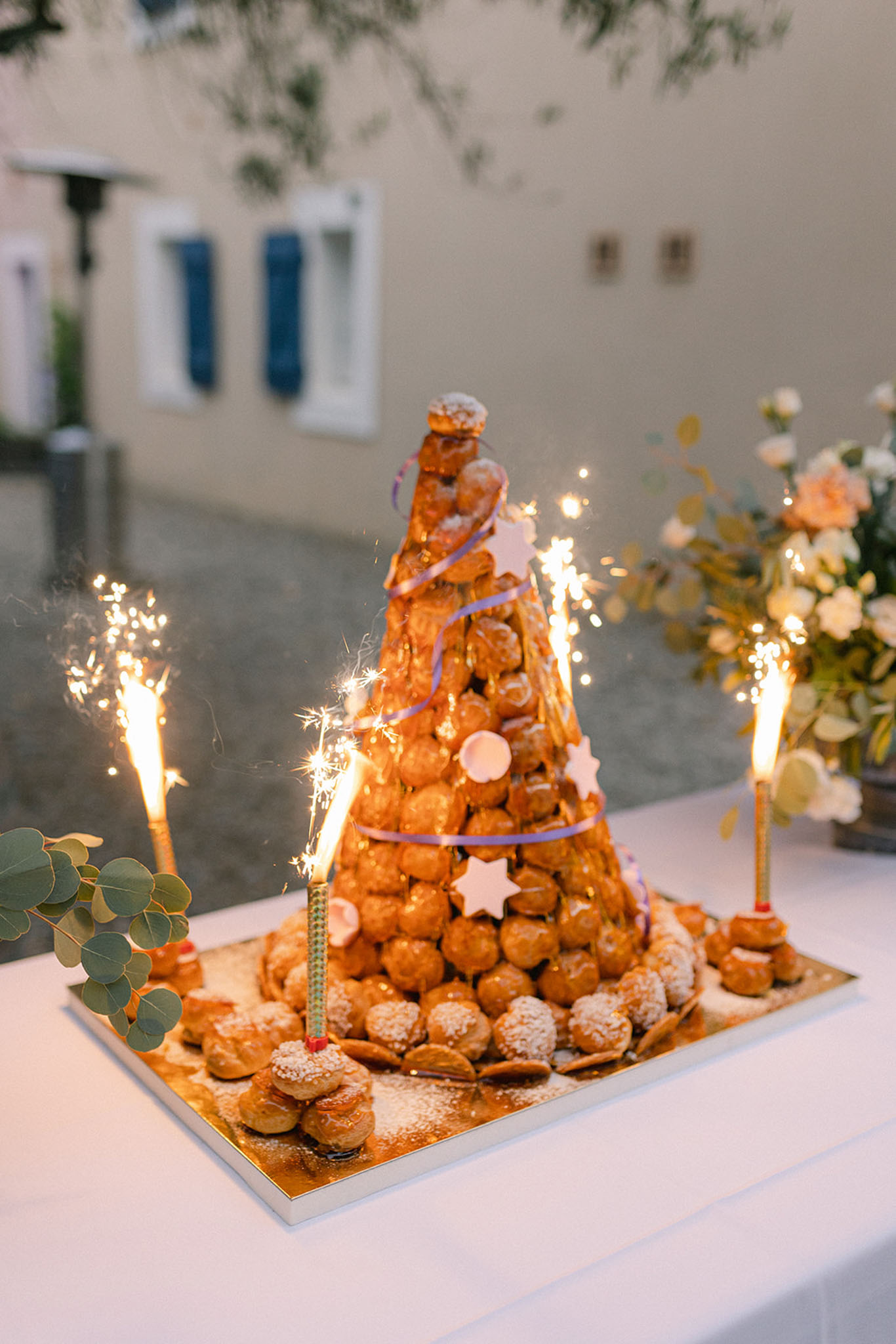 Croquembouche with sparklers, purple ribbon, and star decorations beside cream and peach floral cluster