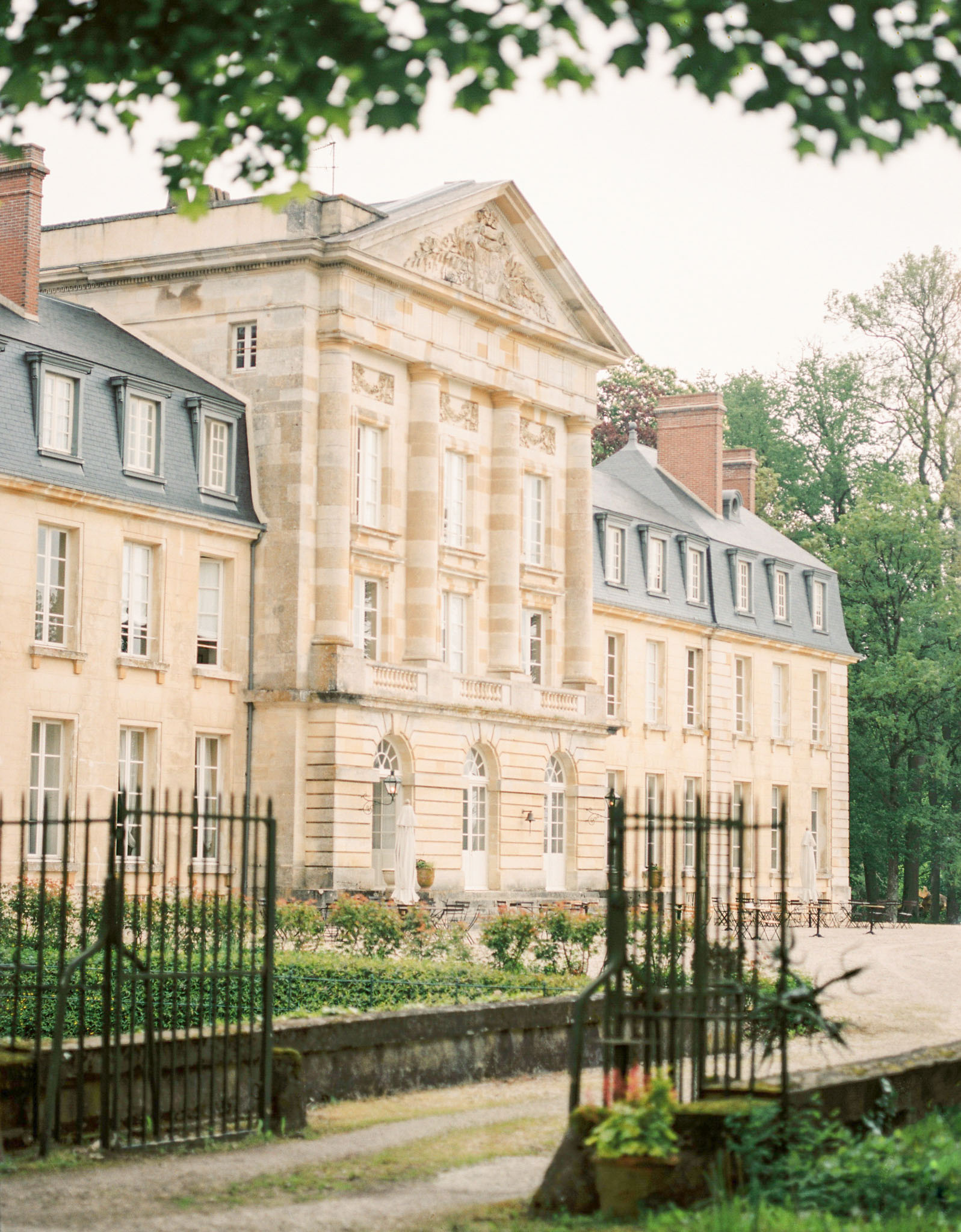Cream limestone chateau with pediment rose parterre and slate mansard roof through iron fence
