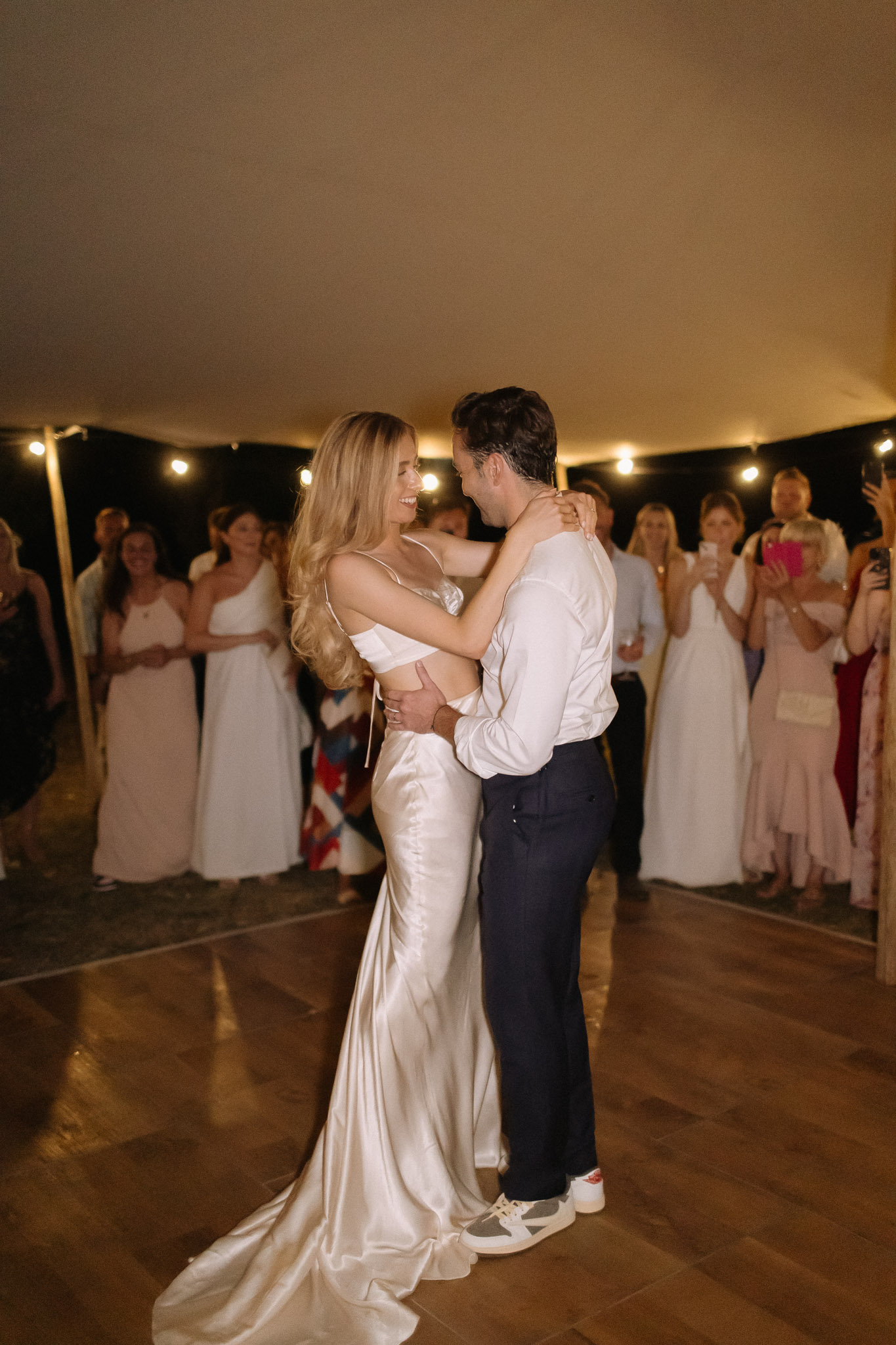 Couple first dance in marquee with globe string lights bride in champagne satin two-piece gown