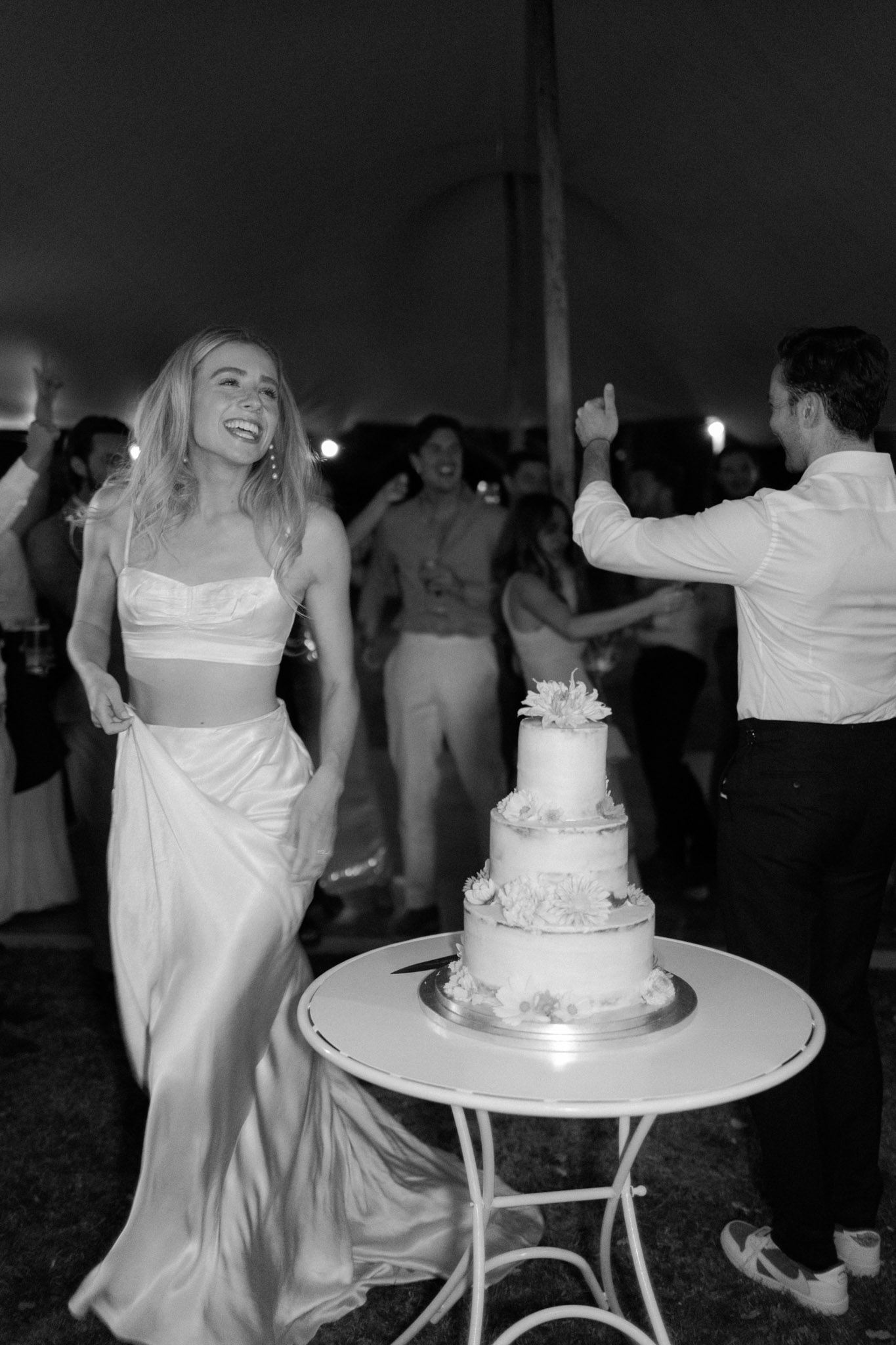 Black and white bride dancing beside three-tier cake with confetti burst and guests on dance floor