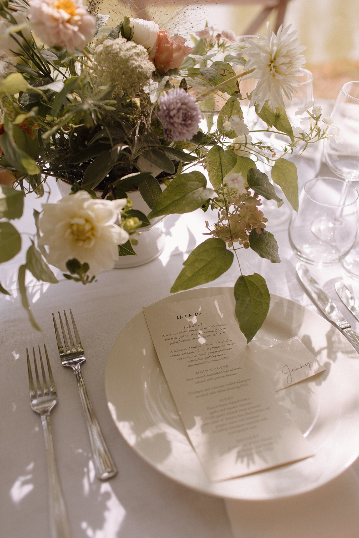 Place setting with menu card and garden-style dahlia, allium, and eucalyptus centerpiece in sunlight