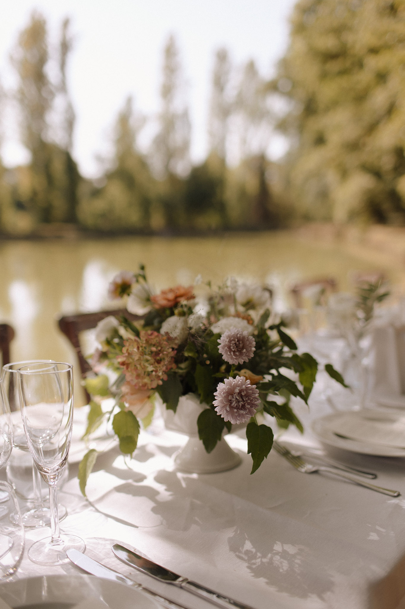 Reception centerpiece of mauve dahlias blush flowers and green foliage in white pedestal compote vase