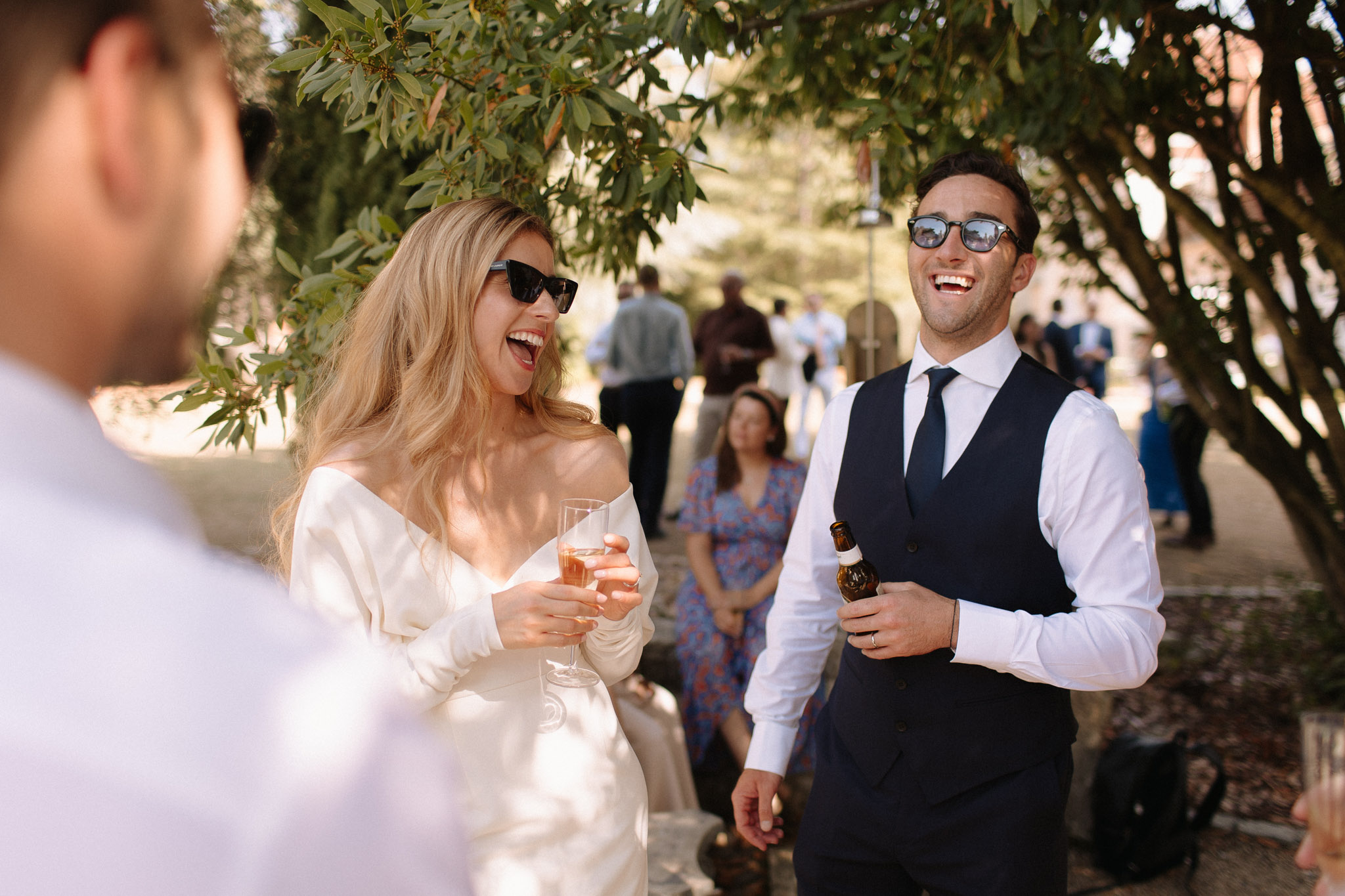 Bride and groom laughing together during cocktail hour, bride holding rose champagne and groom holding a beer