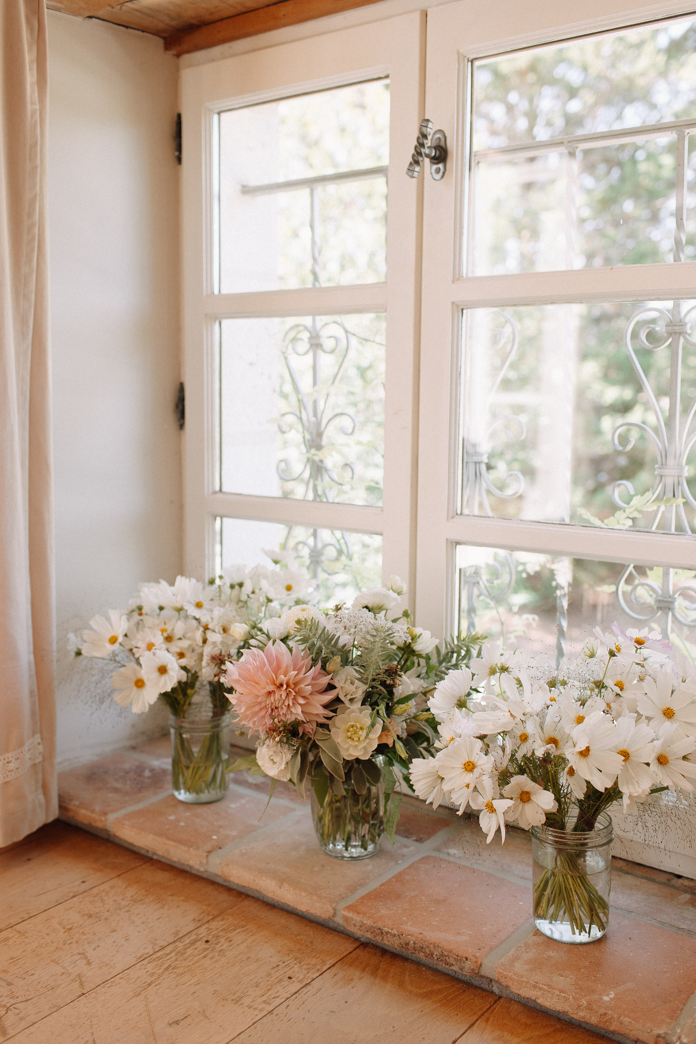 Three mason jar vases on terracotta windowsill with blush dahlia, cream ranunculus, and white cosmos