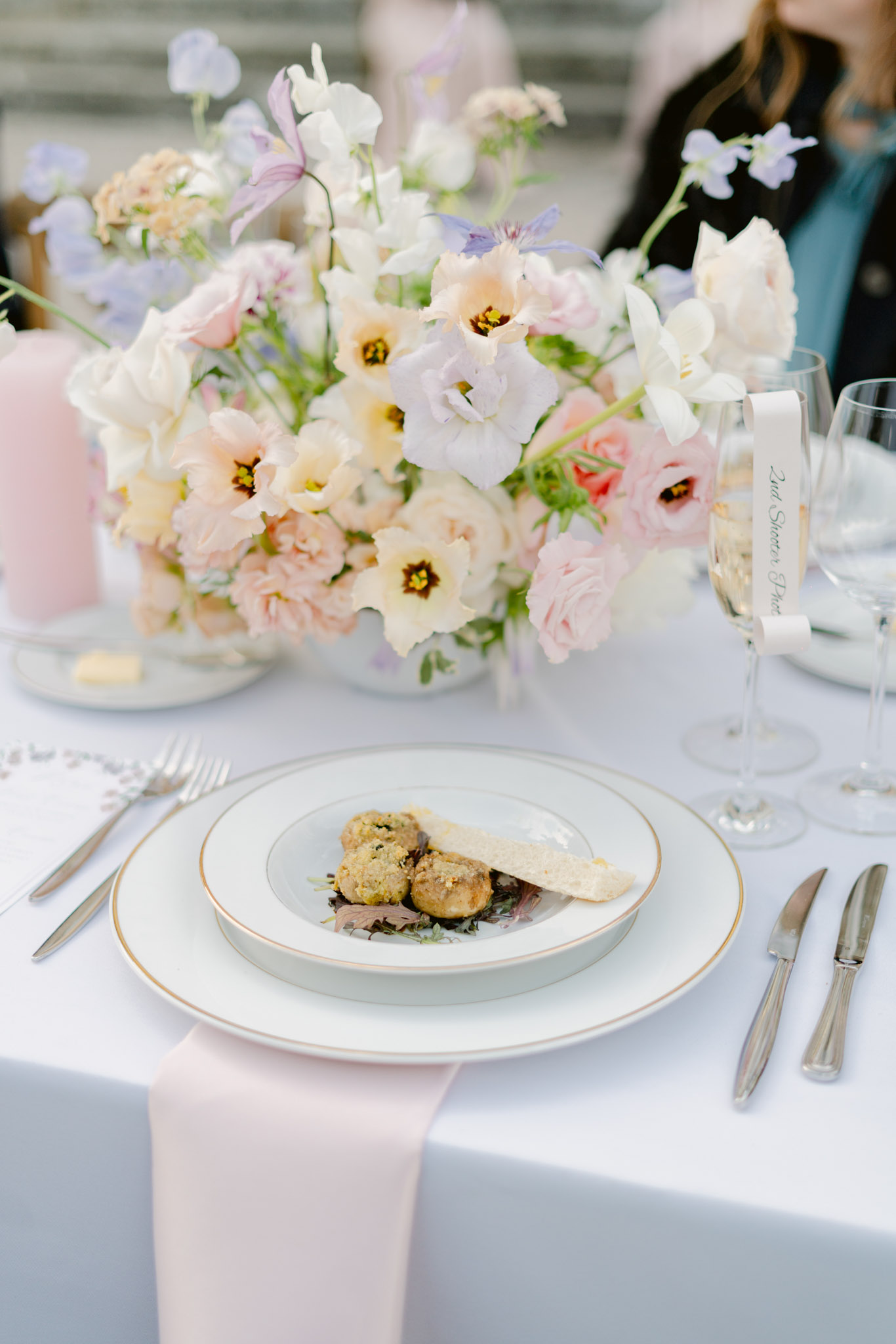 Place setting with gold-rimmed china and blush rose, lavender, and cream tulip centerpiece
