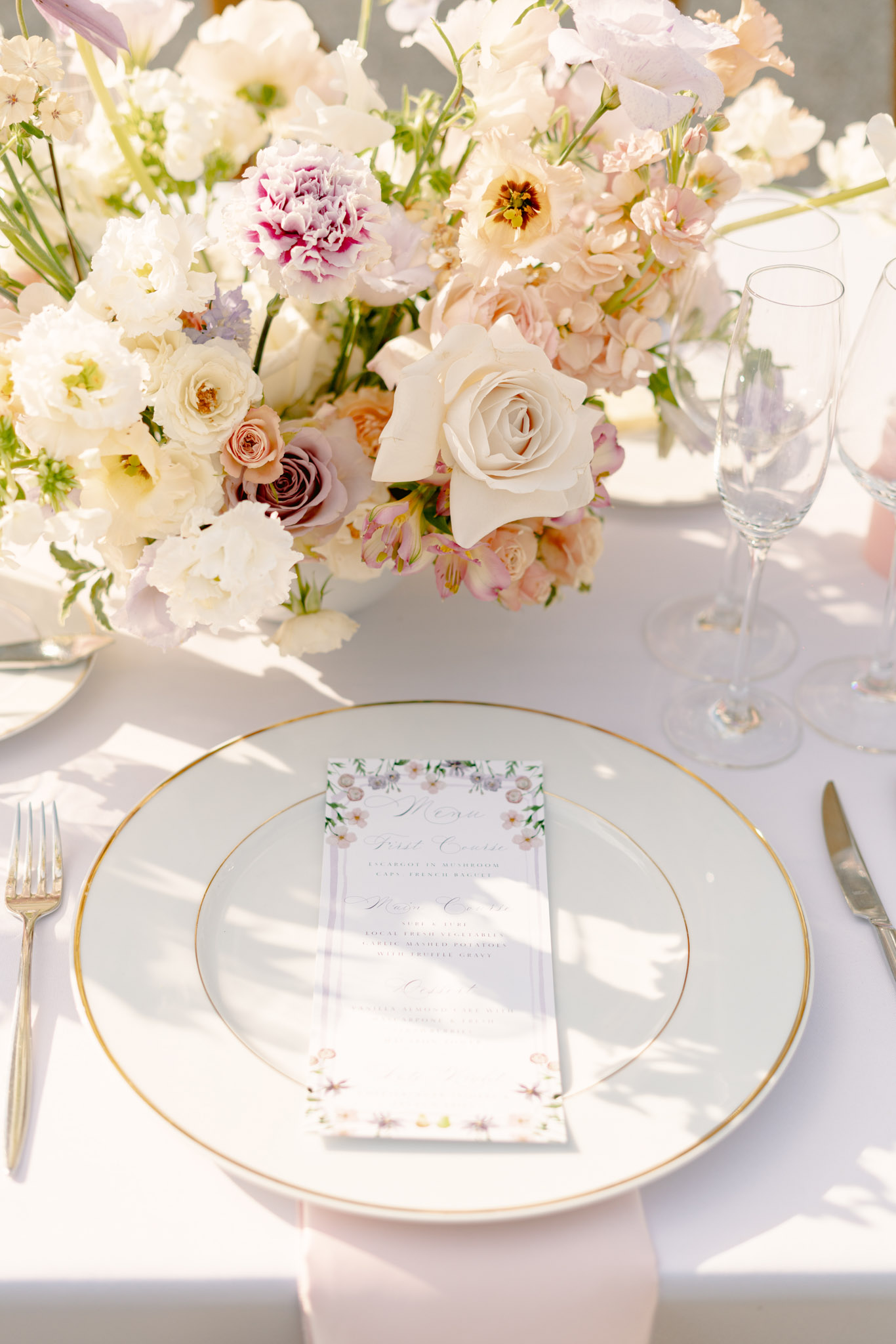Place setting with gold-rimmed charger botanical menu card and lush ivory rose blush and mauve garden-style centerpiece