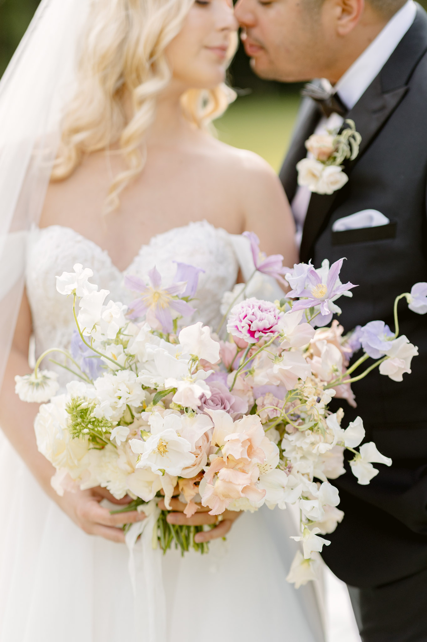 Close-up of couple kissing with oversized pastel bouquet of sweet peas, roses, and clematis