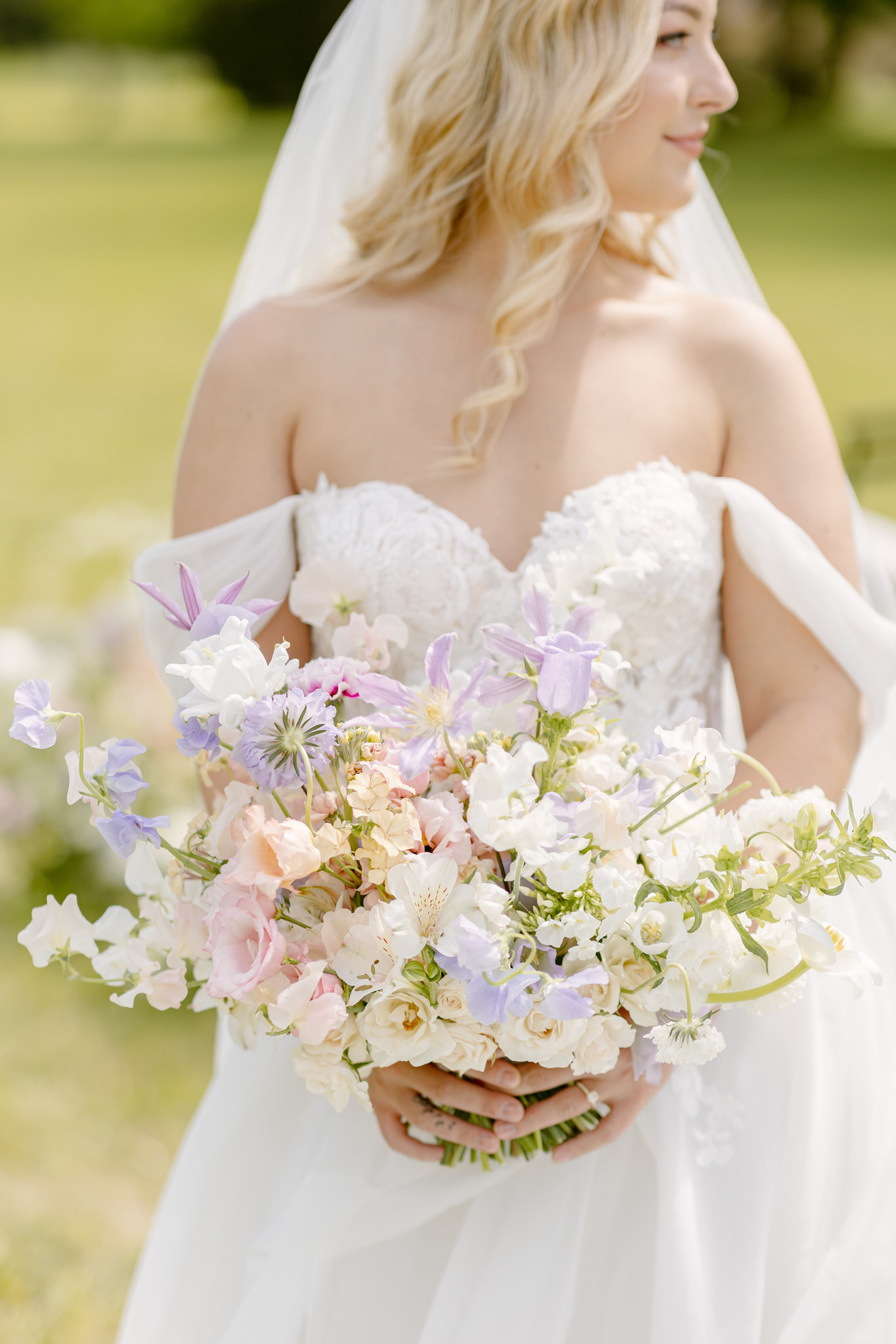 Bride holding pastel garden bouquet of sweet peas roses and clematis with flowing veil outdoors