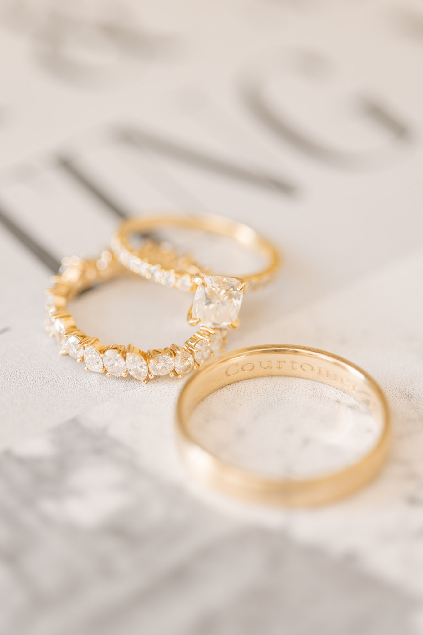 Three yellow gold rings on white marble: oval diamond engagement, pave diamond band, and plain band