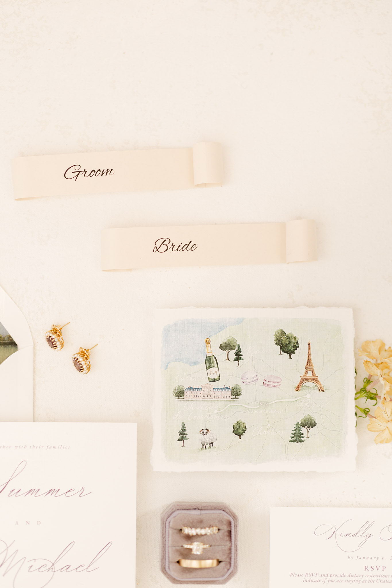 Wedding stationery flat lay with watercolor France map, calligraphy place cards, and velvet ring box