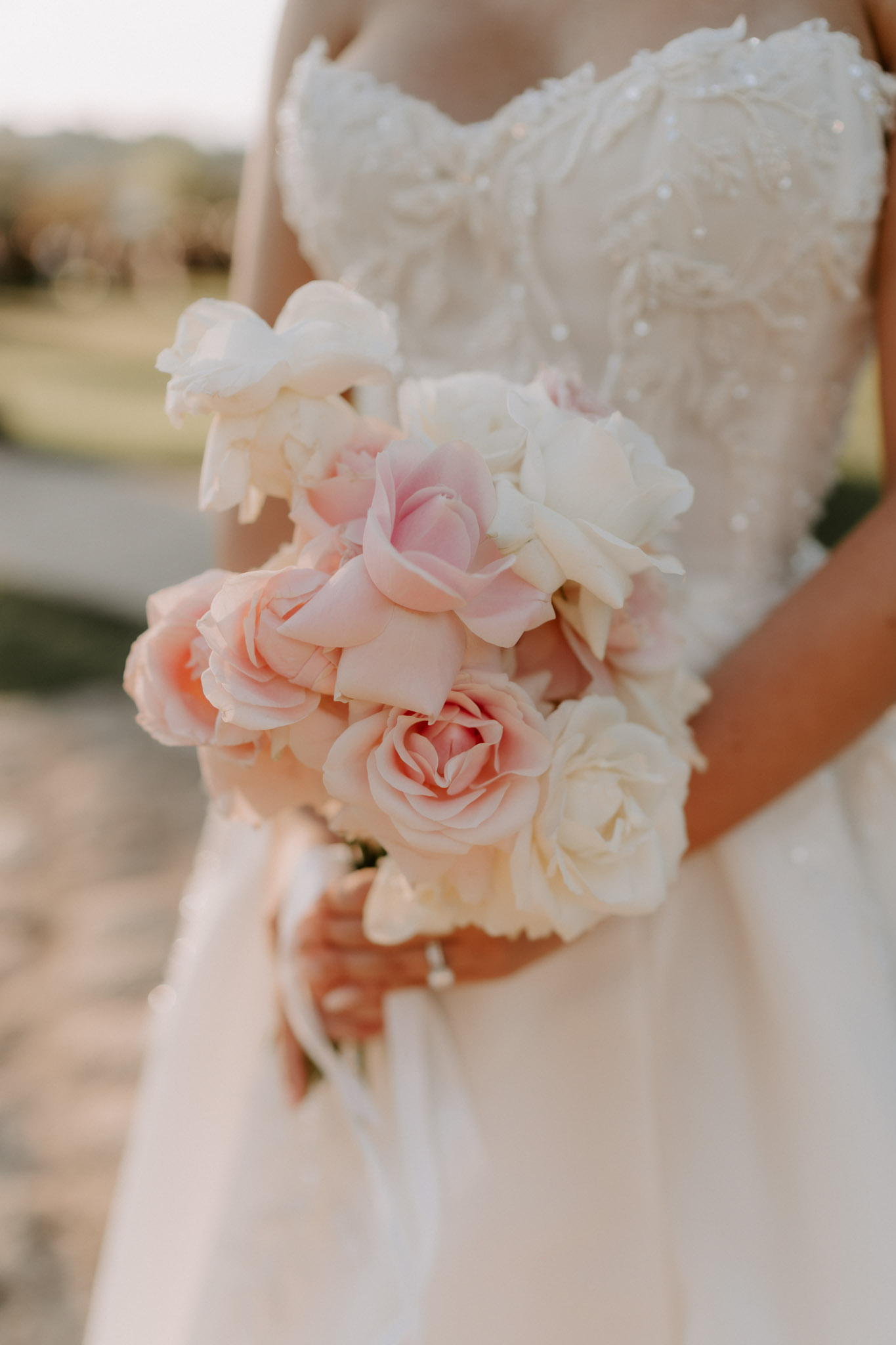 Close-up bride holding blush pink and ivory rose bouquet in strapless gown with pearl and floral beaded bodice