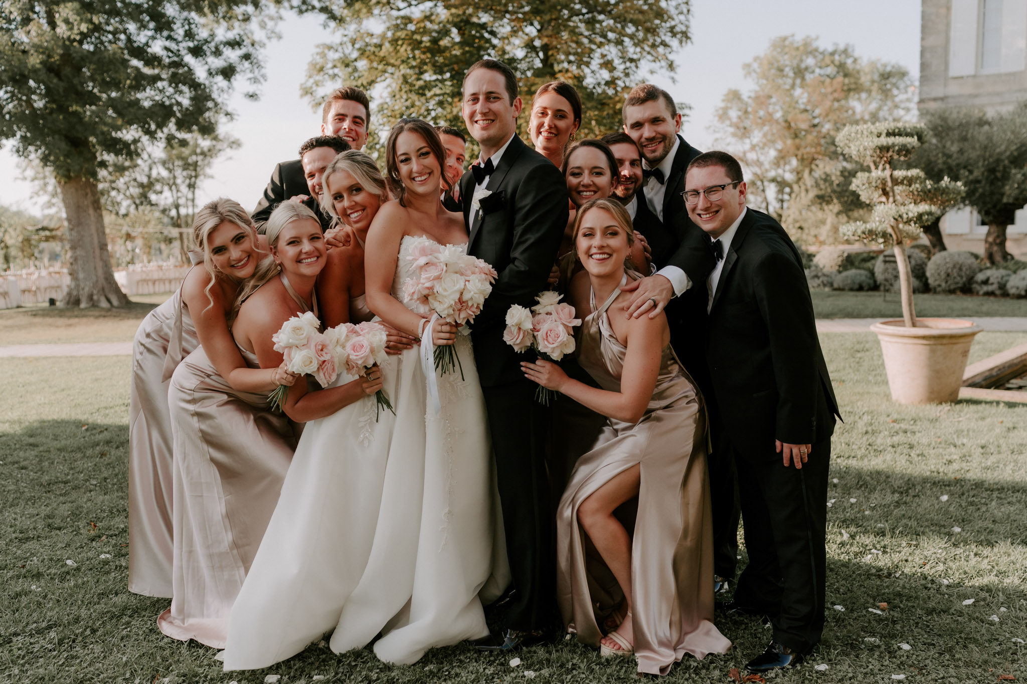 Bridal party group portrait on lawn with bridesmaids in champagne-gold gowns and groomsmen in black tuxedos