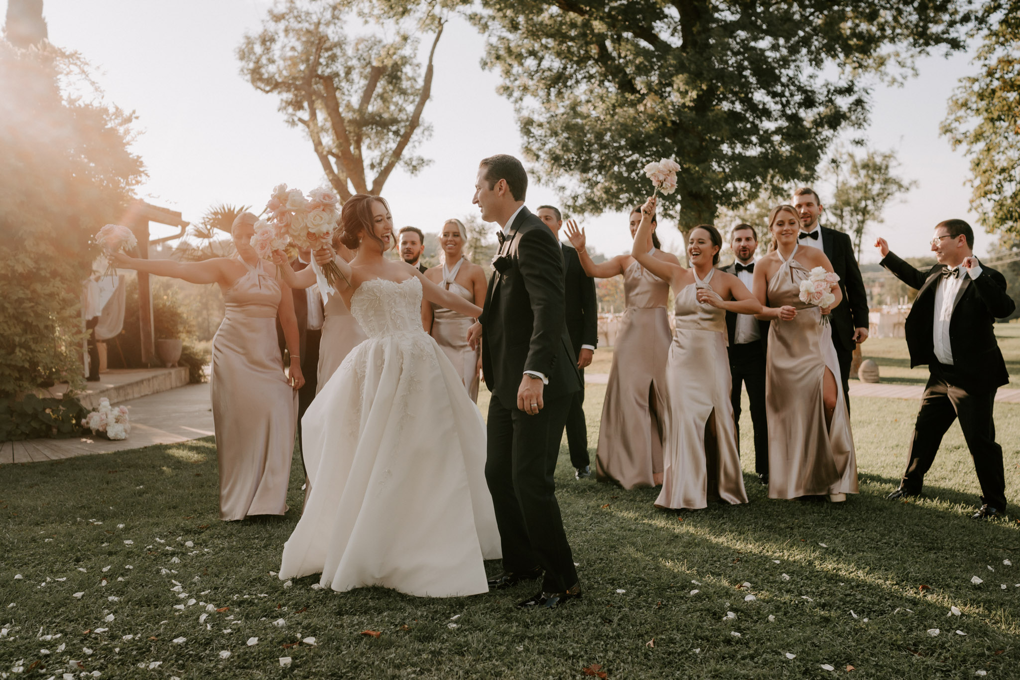 Bridal party celebrating at golden hour with champagne-gold bridesmaids and tuxedoed groomsmen