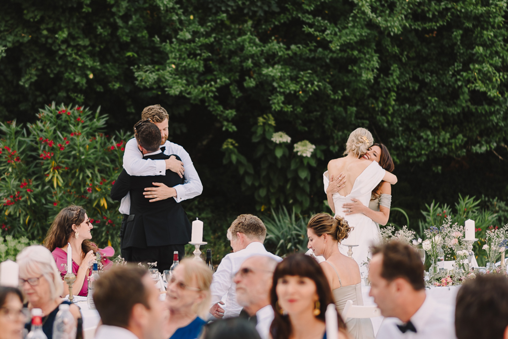 Post-speech embrace as bride and groom hug guests at candlelit al fresco reception dinner