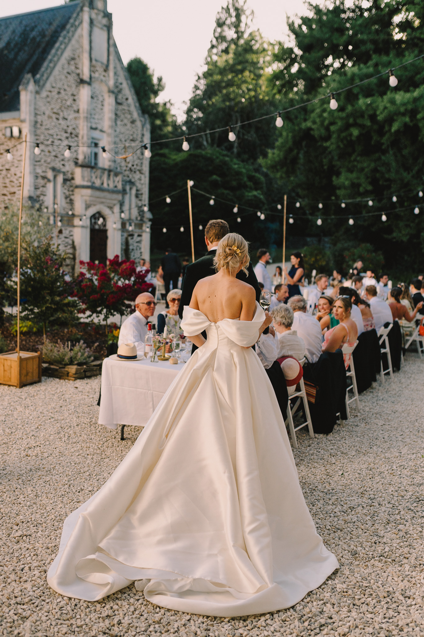 Bride with dramatic back bow and groom facing banquet guests under festoon lights at Gothic chateau