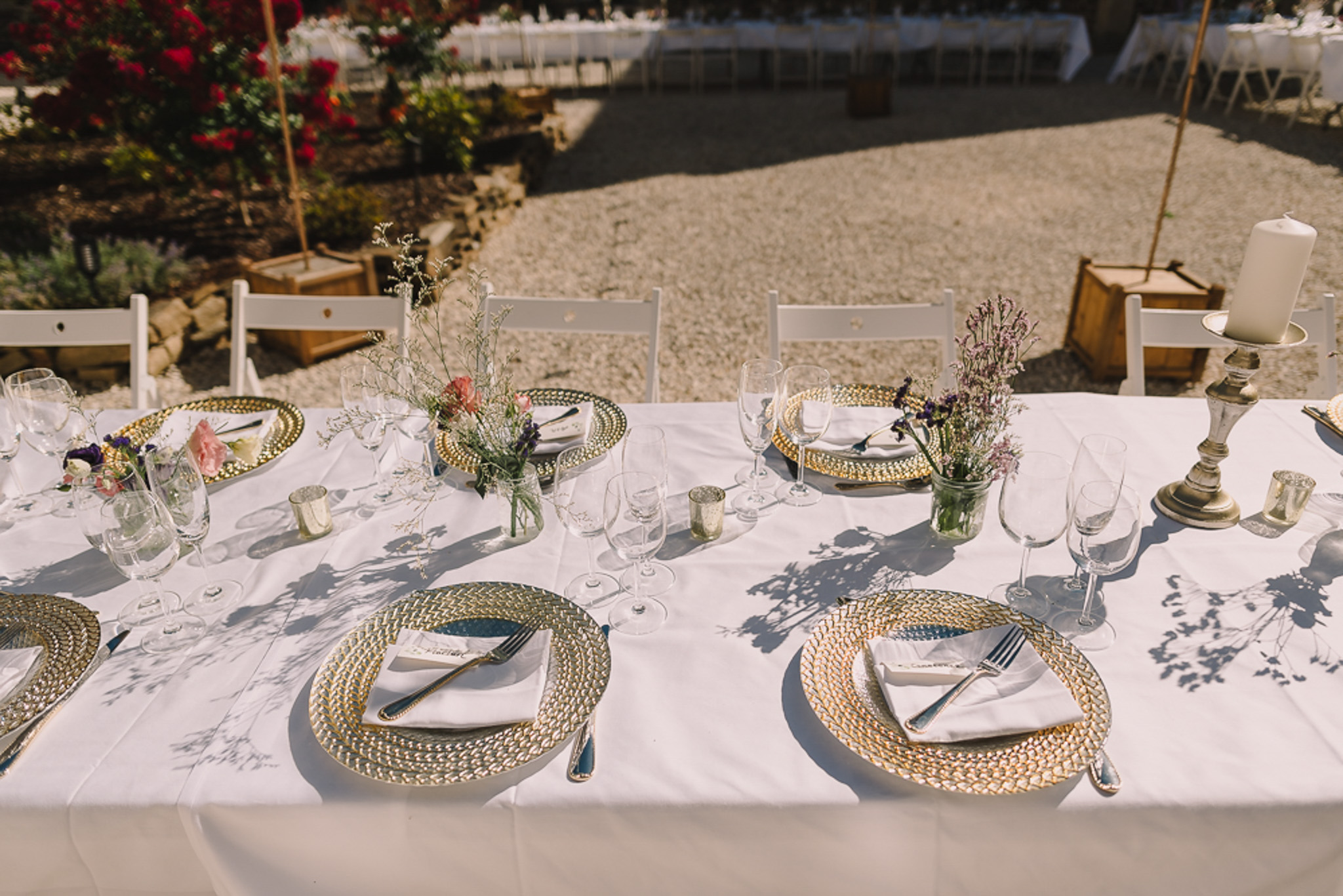 Long reception table with gold charger plates, blue plates, wildflower centerpieces, and mercury glass votives