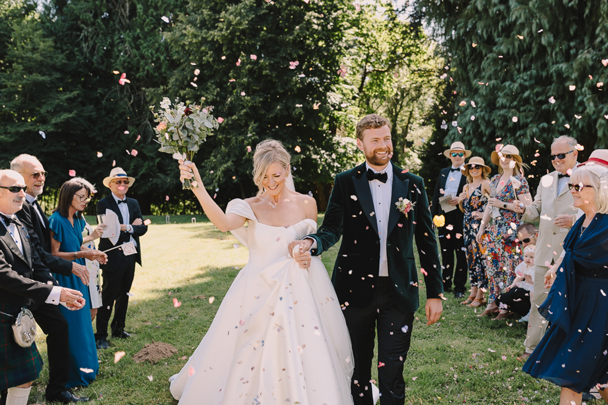 Couple exits through pink and peach petal confetti tunnel with groom in green velvet tuxedo jacket
