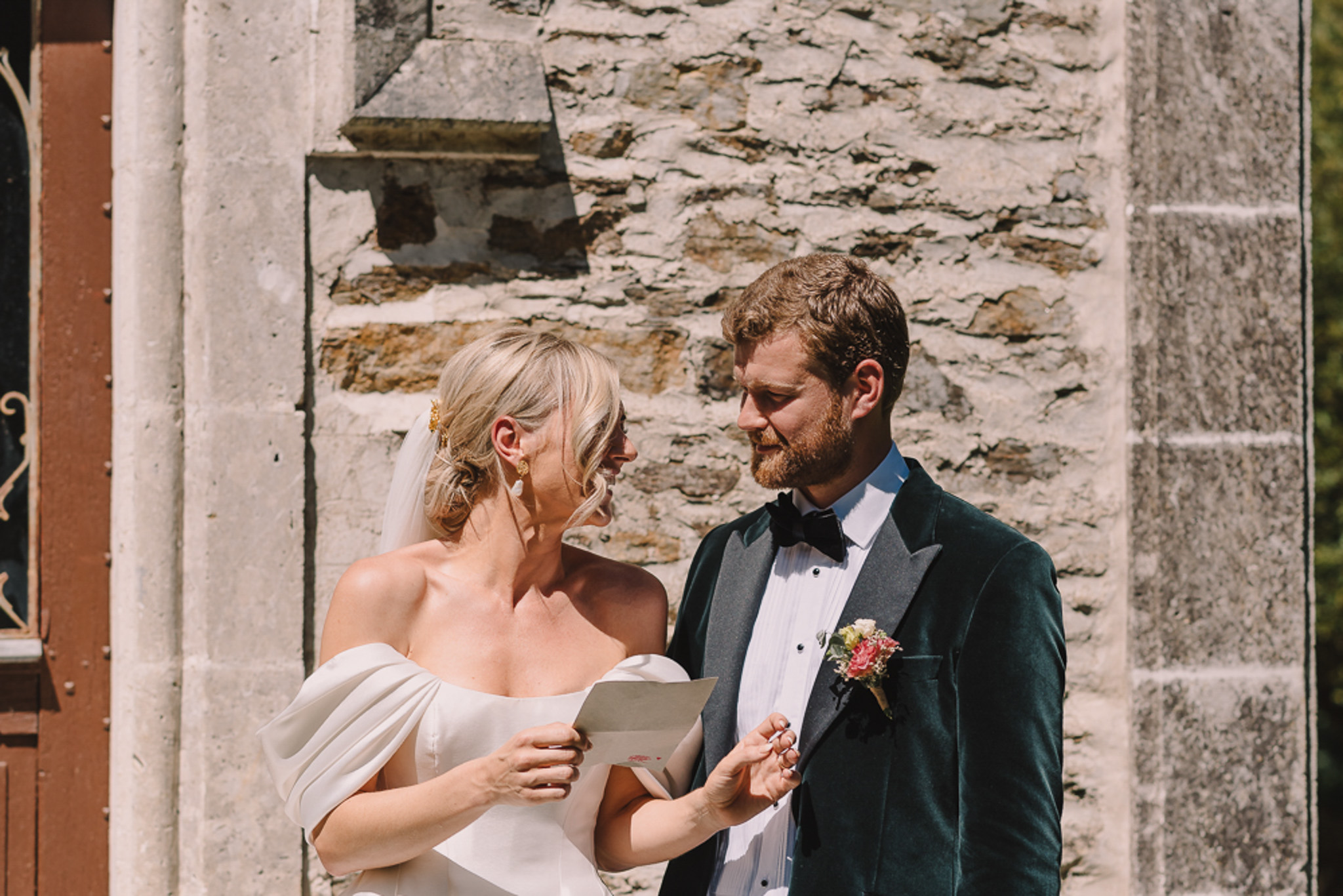 Couple reading note at stone doorway, groom in forest green velvet jacket, bride in cathedral veil