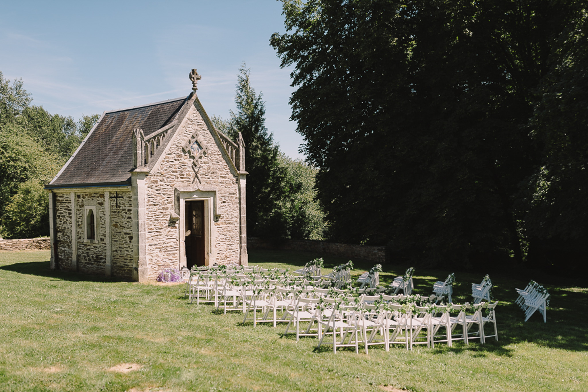Pre-ceremony setup with white chairs in semicircle facing Gothic stone chapel decorated with greenery garlands