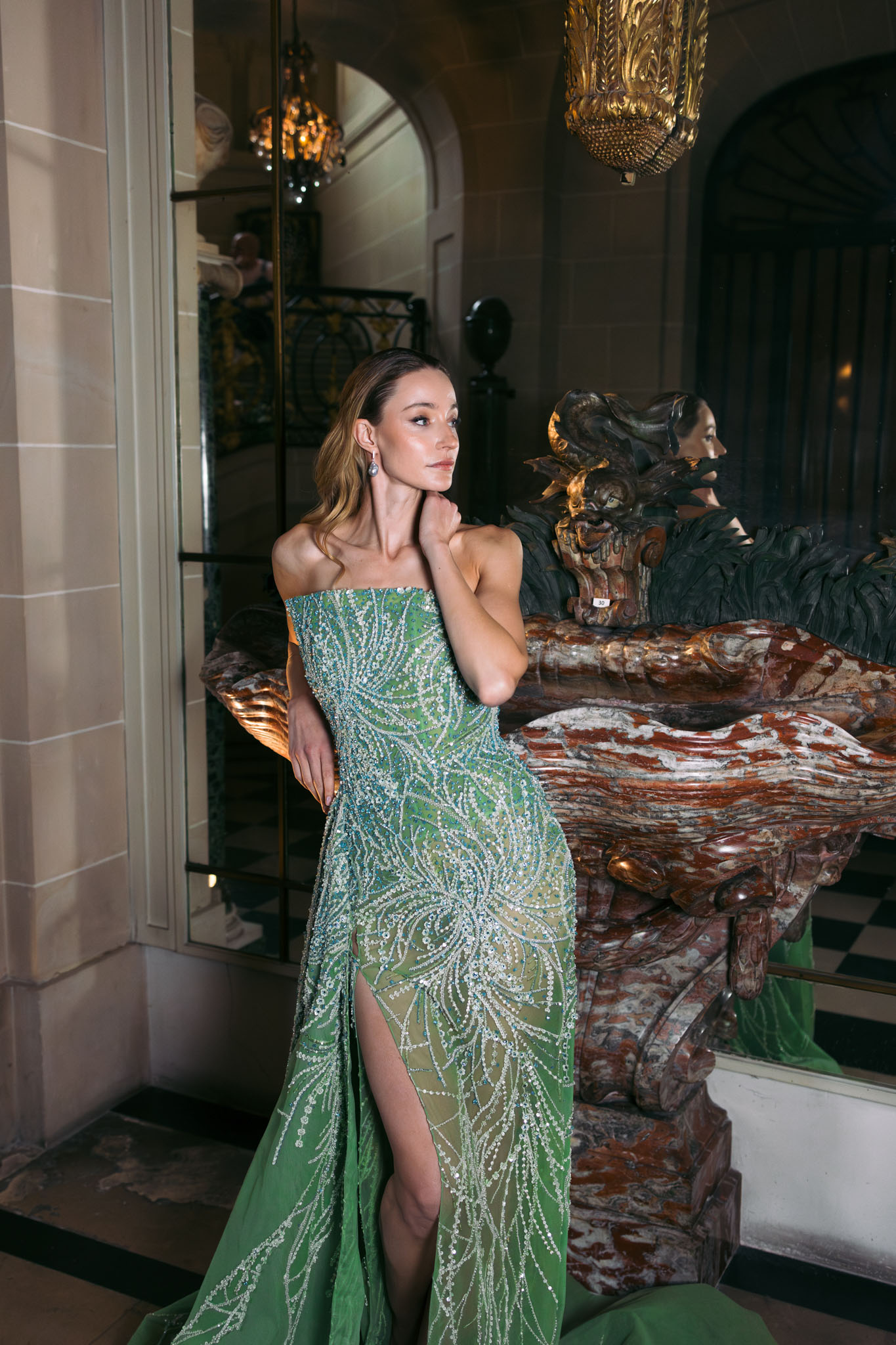 Woman in sage green beaded strapless gown standing in ornate Parisian interior with gold lanterns