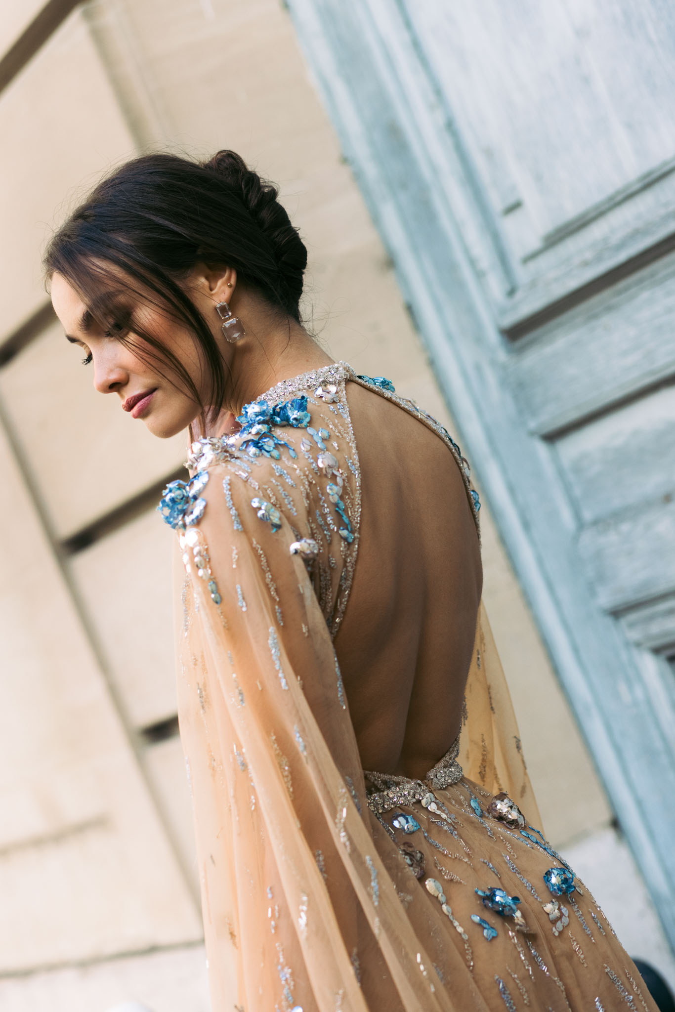 Back detail of bridal gown with blue floral appliques and silver beading, bride in low braided updo with crystal earring