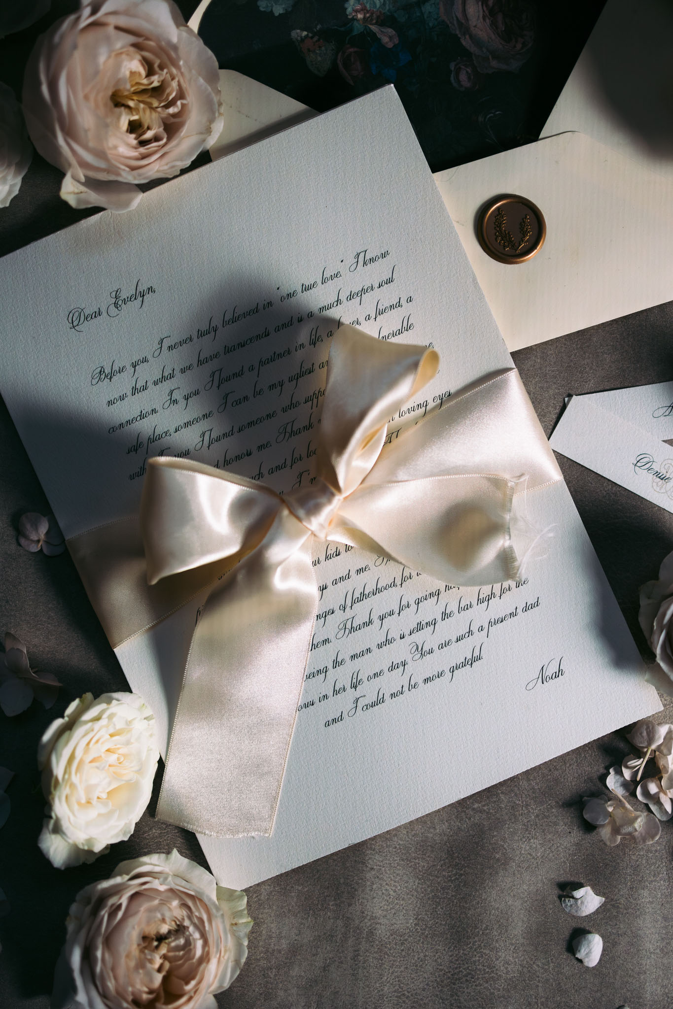 Wedding stationery flat lay with handwritten vow letter, teal envelope, gold wax seal, and garden roses