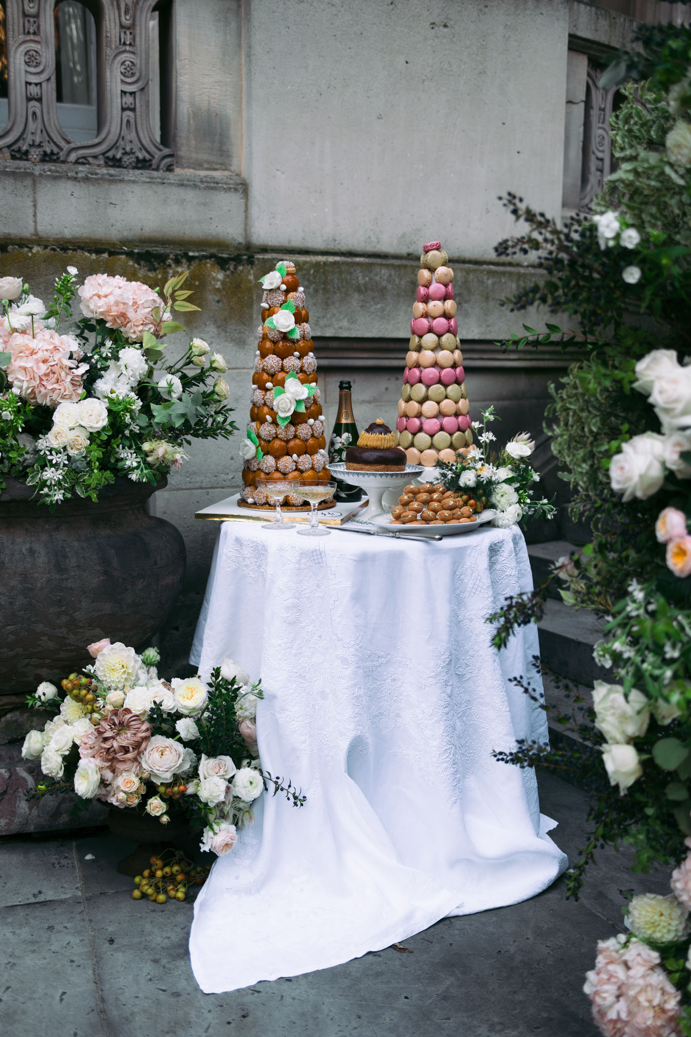 Dessert table with croquembouche and macaron tower chocolate tart blush rose arrangements against ornate stone facade