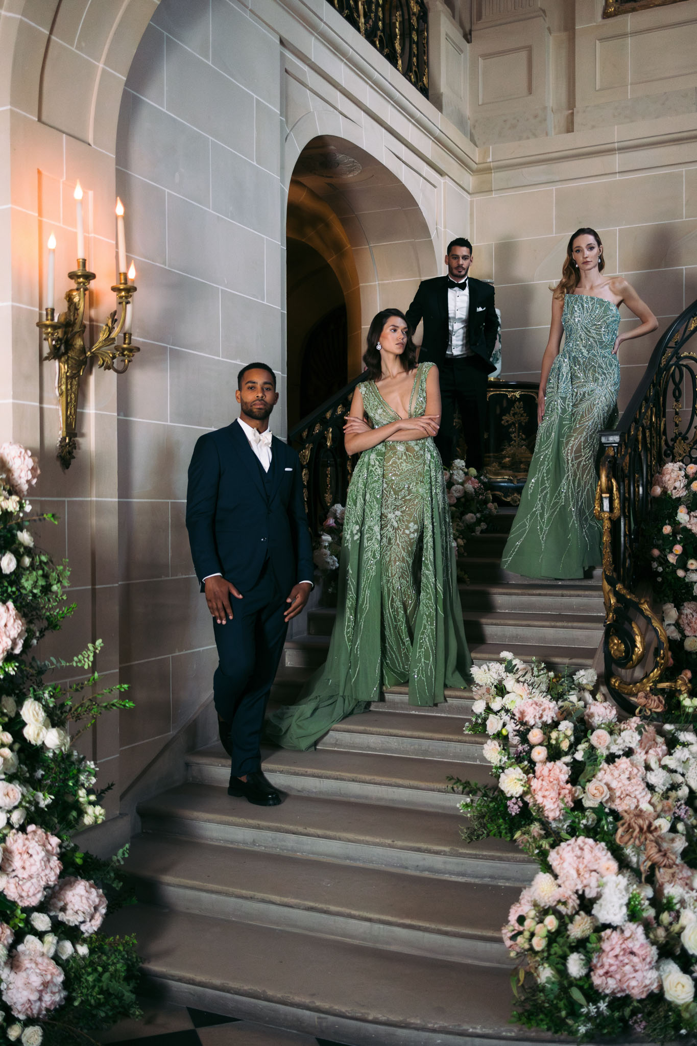 Four-person editorial portrait on ornate chateau staircase with sage green beaded gowns and blush hydrangea arrangements