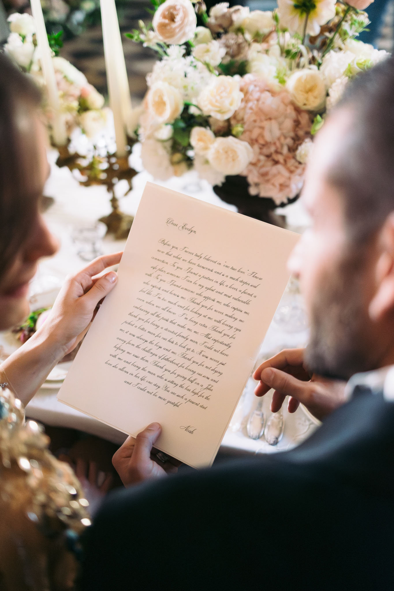 Couple reading handwritten letter at table with blush hydrangea centrepiece and gold taper candle holders