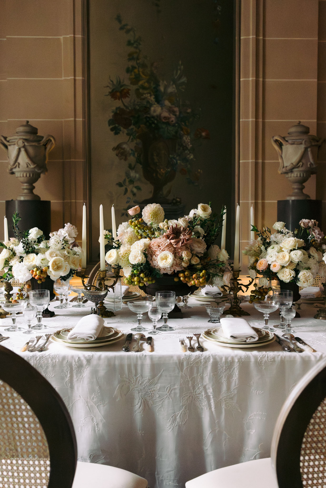 Ivory and dusty rose dahlia centerpieces with brass candelabras before floral mural in stone-panelled salon